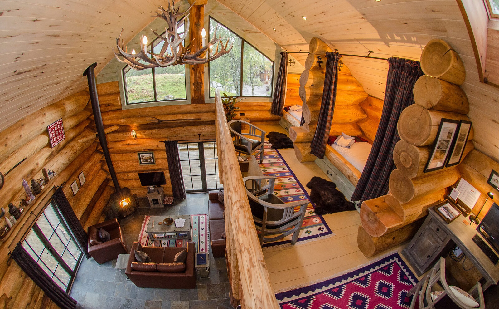 From the mezzanine under an antler chandelier, down into a cabin's living room, the log beds curtained in the wall.