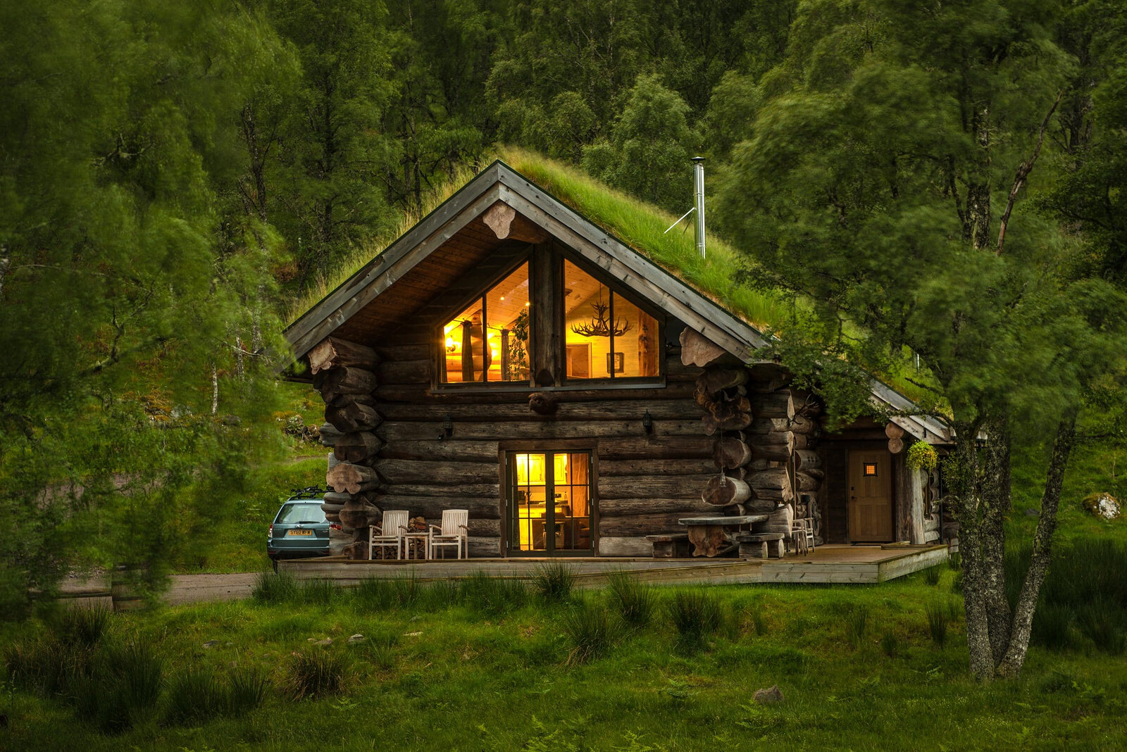 Loxia's gable lit gold at dusk among the green birches, chairs set out on the deck.