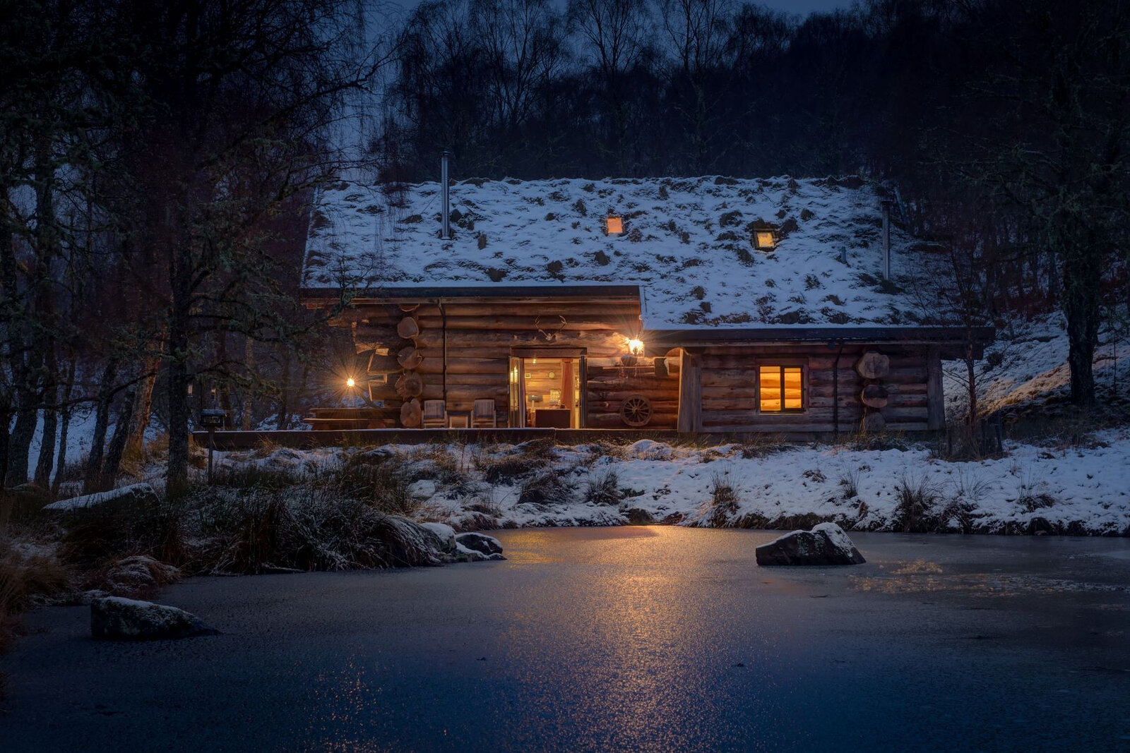 Loxia at night in snow, its windows lit across the frozen pond.