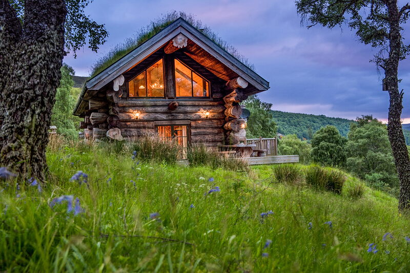 Parus on its slope at dusk above bluebells in the grass, its gable windows lit.