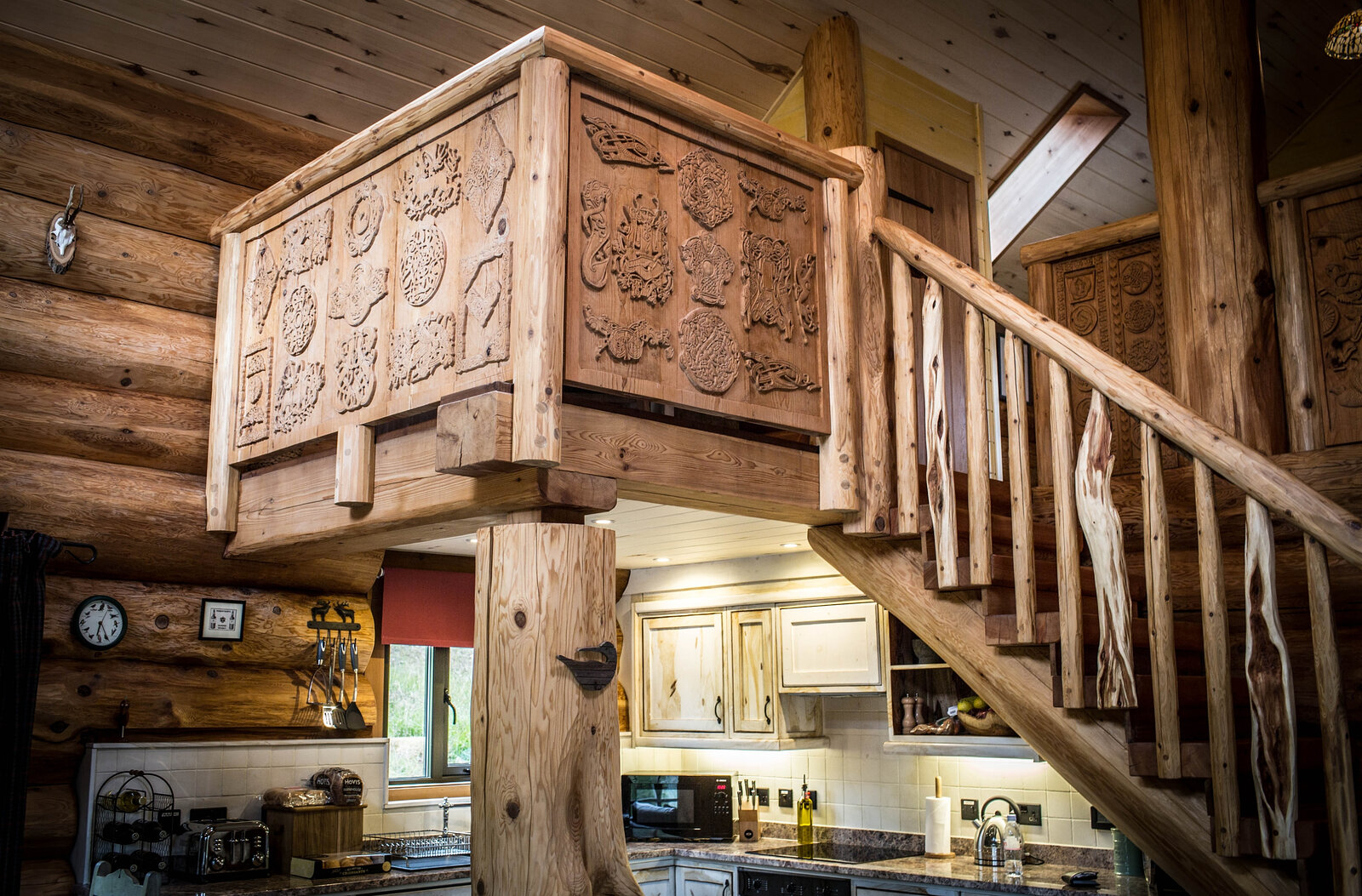 Strix's carved mezzanine standing over the kitchen, the log stair climbing beside it.