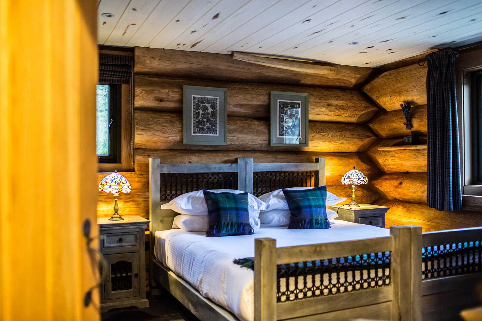 Strix's bedroom through the door: a carved bed with green tartan cushions and two stained-glass lamps.