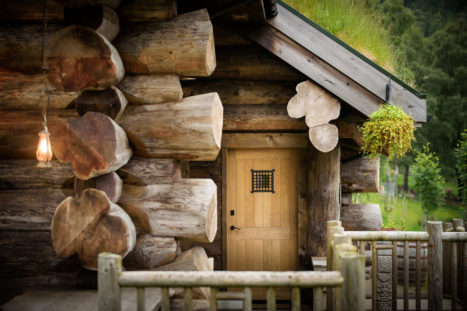 Strix's oak door with a small iron grille, set among the great round log ends, a hanging basket by the rail.