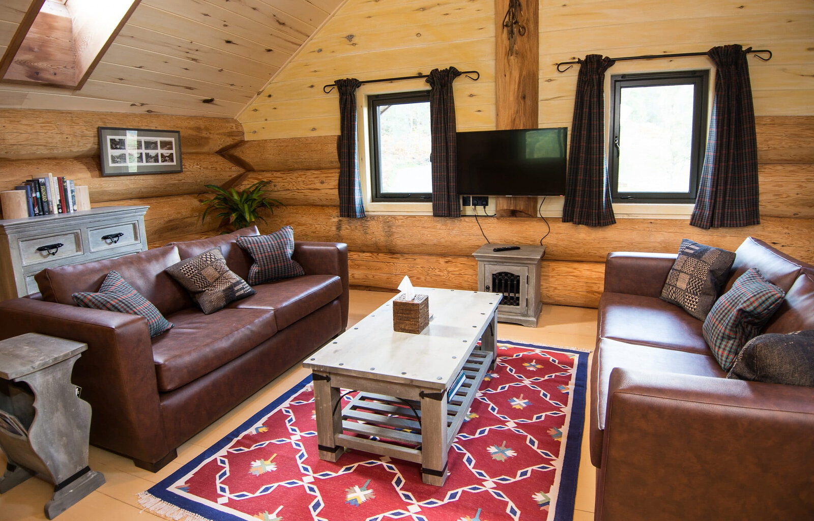Sylvia's upstairs sitting room under the boards: leather sofas on a red rug, windows either side of the TV.