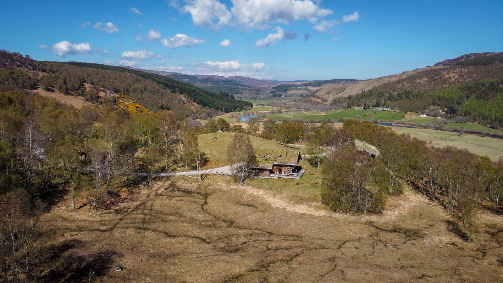 Looking down the glen in spring from the hill above a turf-roofed cabin, the river winding through fields.