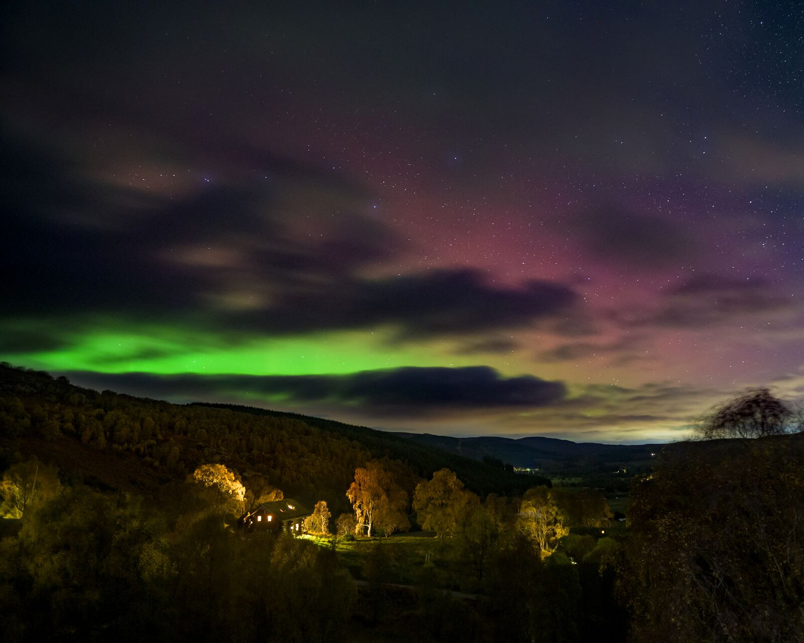 The Northern Lights green and pink over the dark glen, the cabins' lights among the trees below.