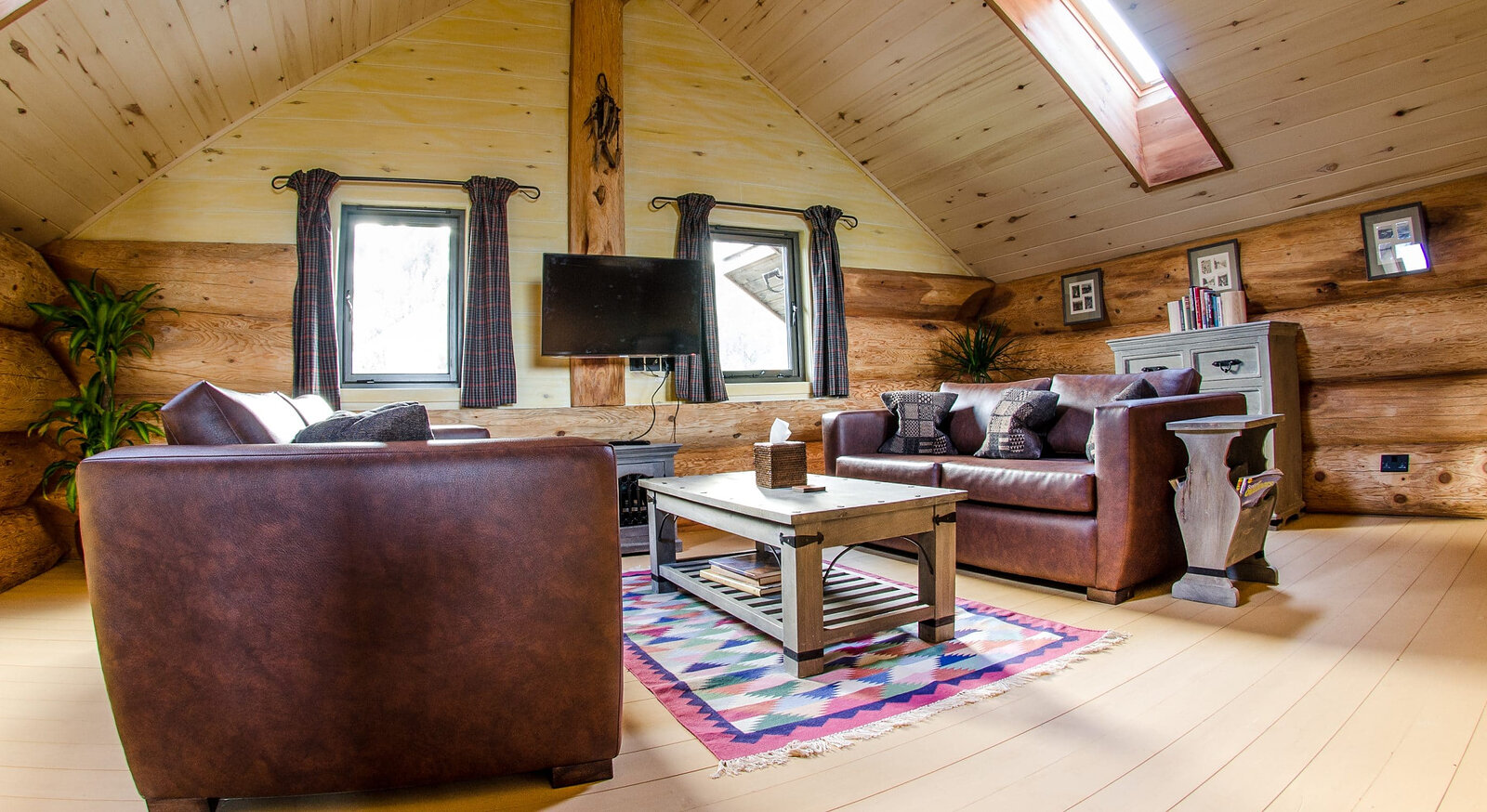 An upstairs sitting room under the boards and a skylight, leather sofas on a bright rug.