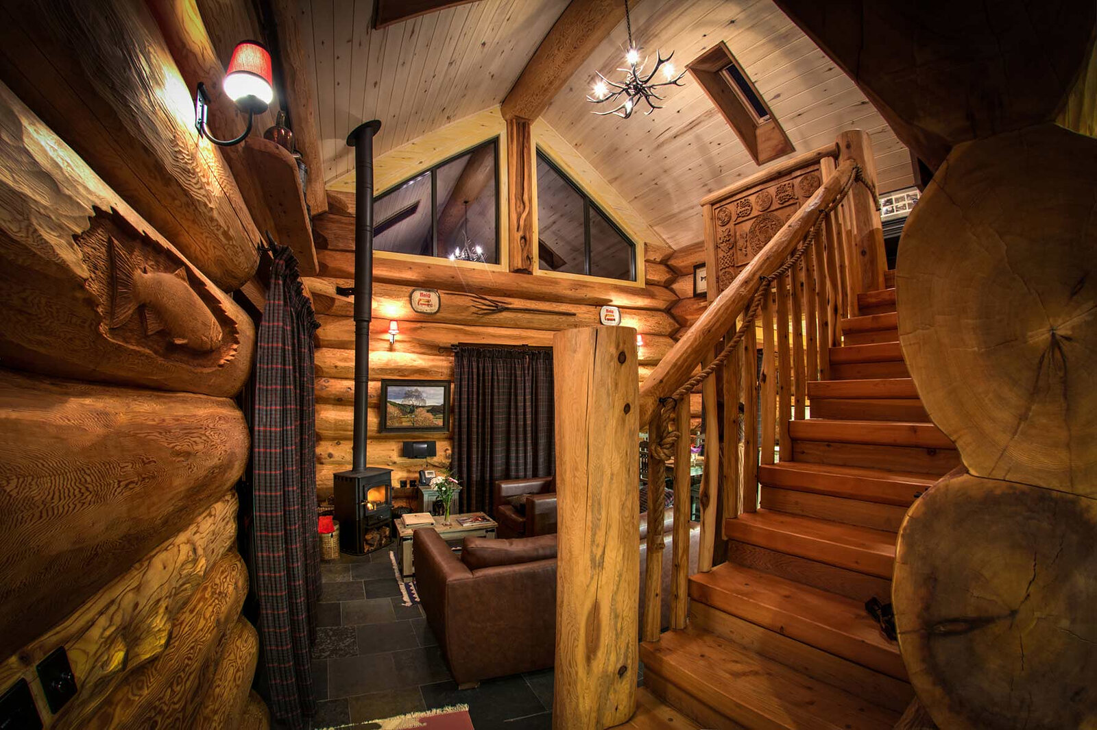 Tringa's log stair and carved rail rising past the living room, an antler chandelier under the gable.