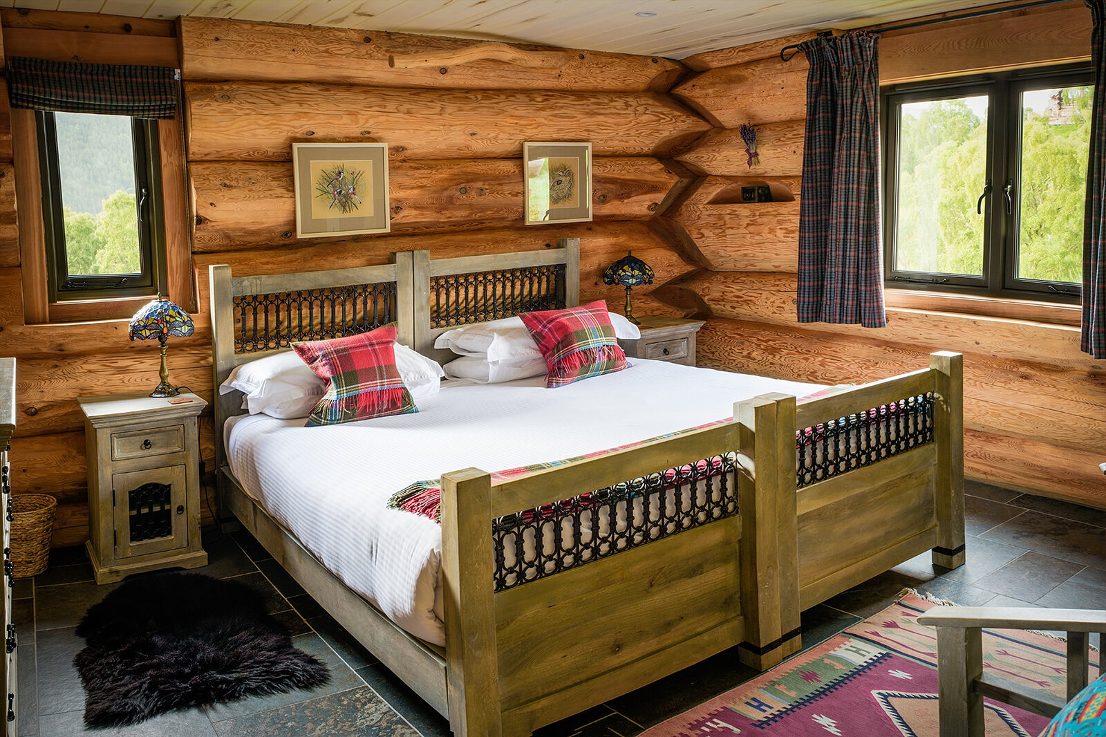 Tringa's bedroom: a carved bed with red tartan cushions, stained-glass lamps and windows onto the birches.