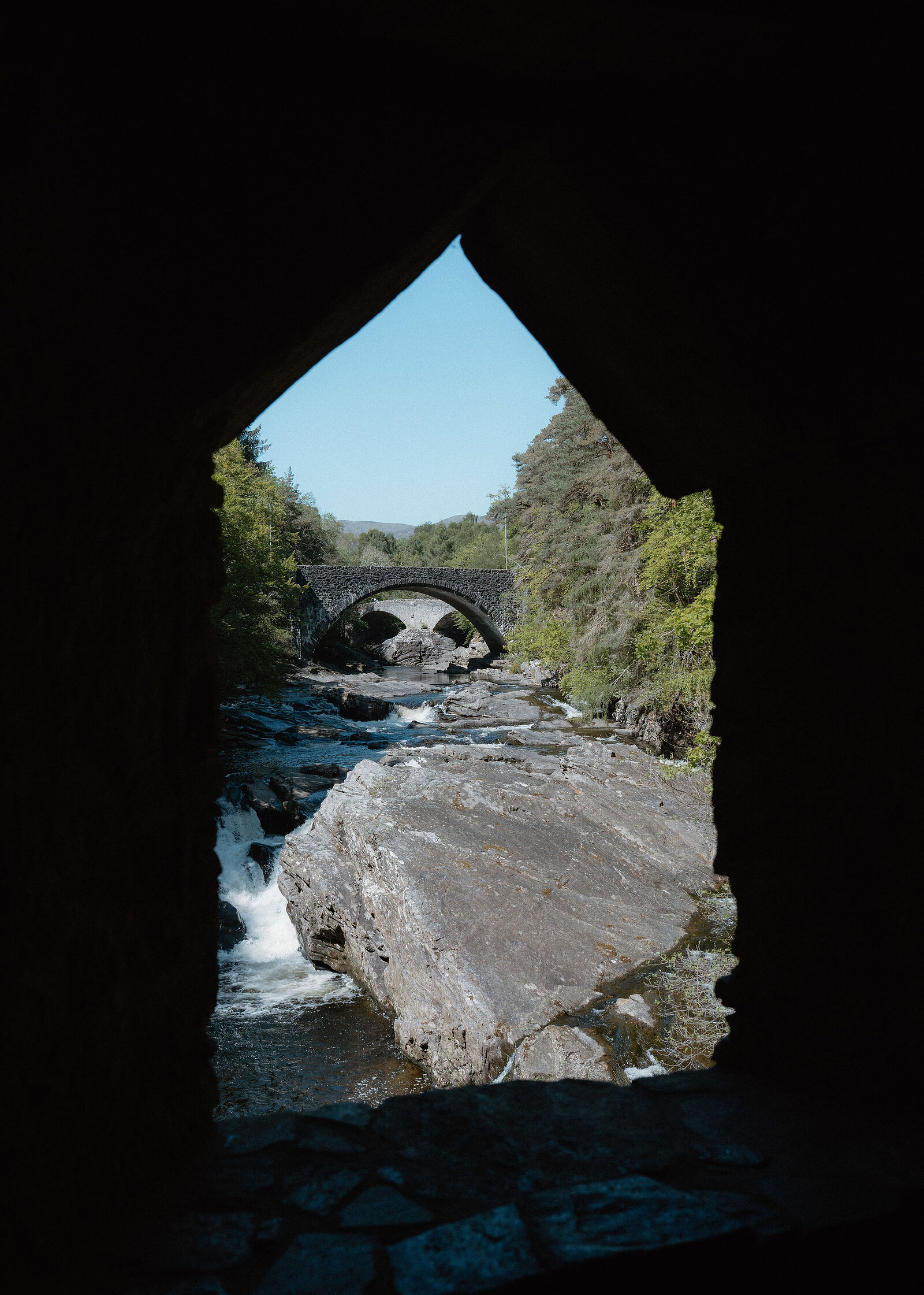 The falls and a great slab of rock framed by the pointed window of the stone summerhouse, a bridge in the distance.
