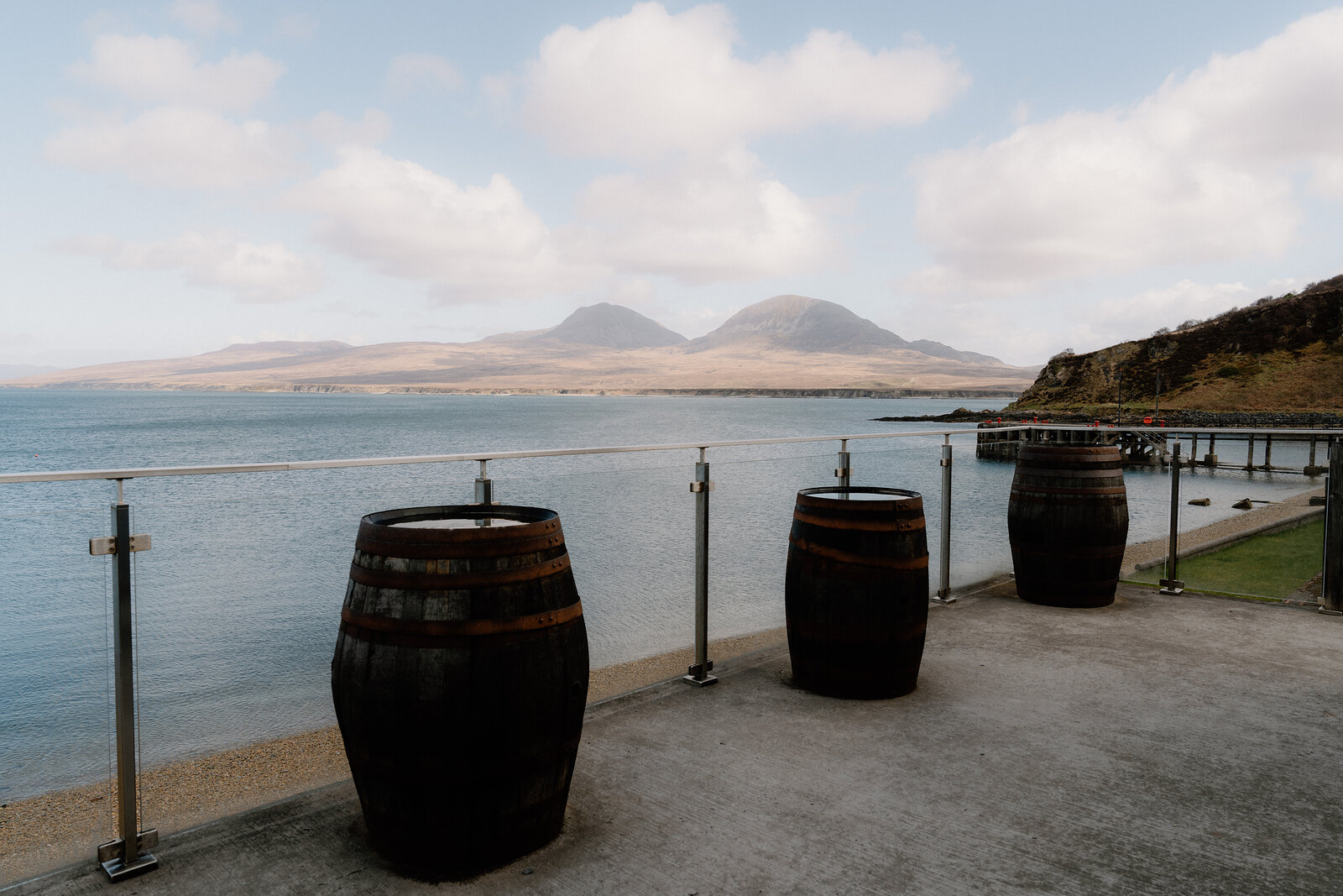 Whisky casks serve as tables on a terrace overlooking the sea and mountains.