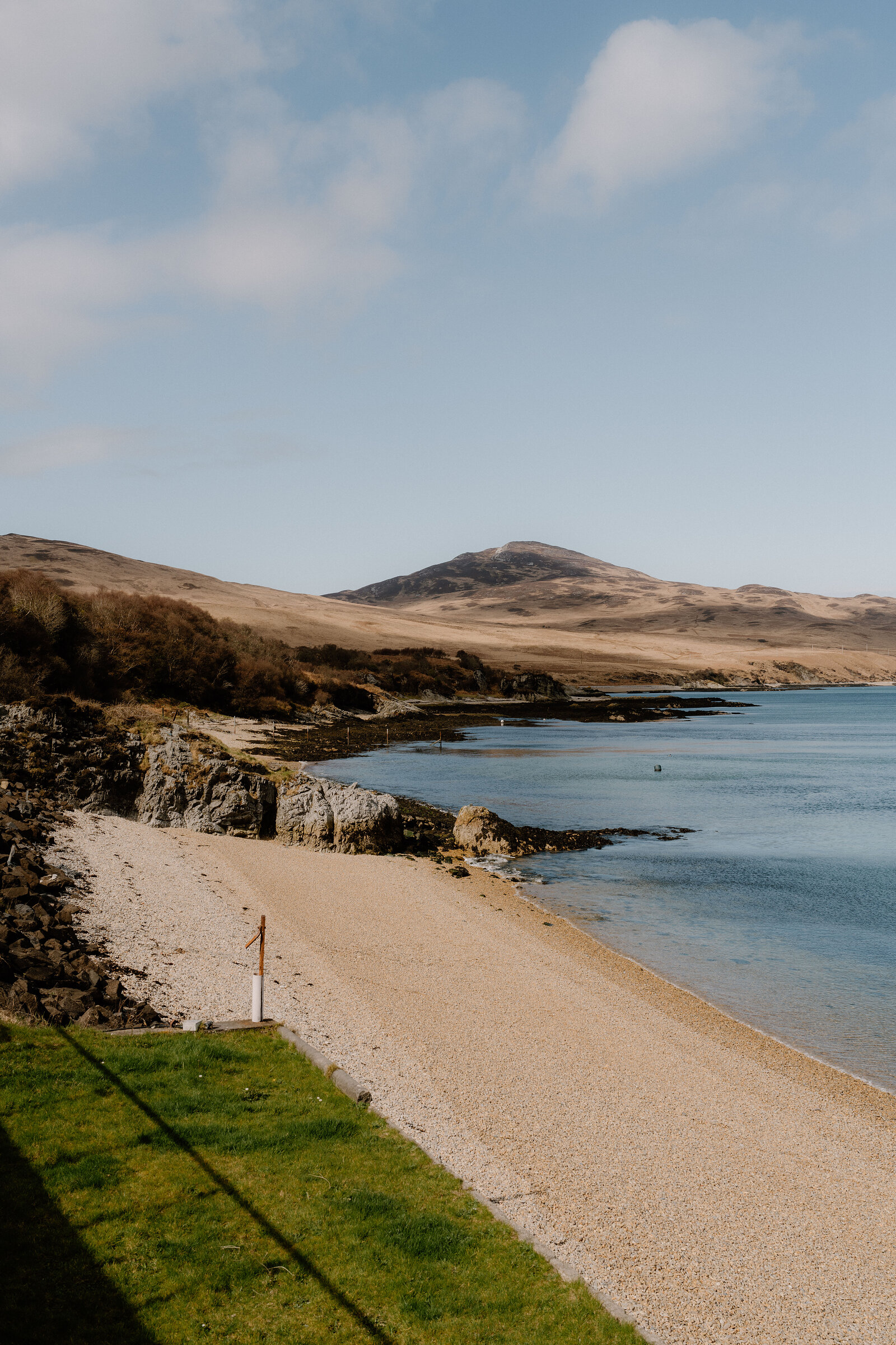 A shingle beach curves beneath a hill, a signpost marking the shore.