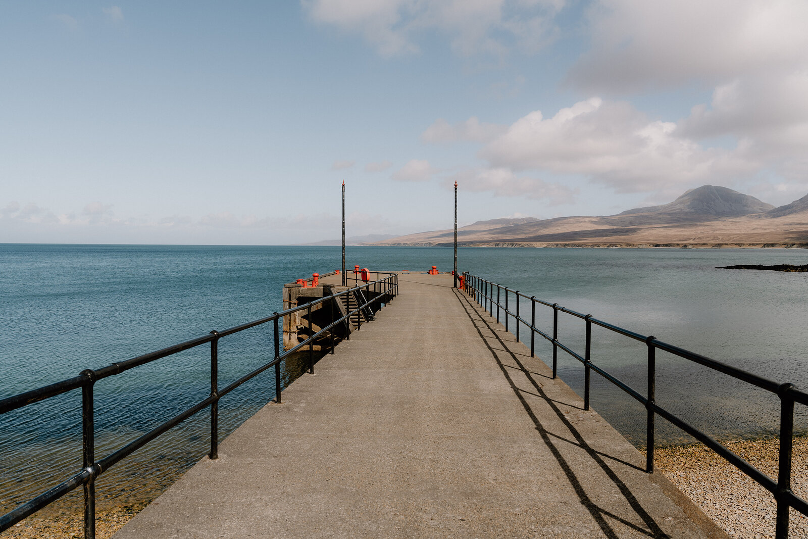A stone pier extends into the sea before distant mountains.