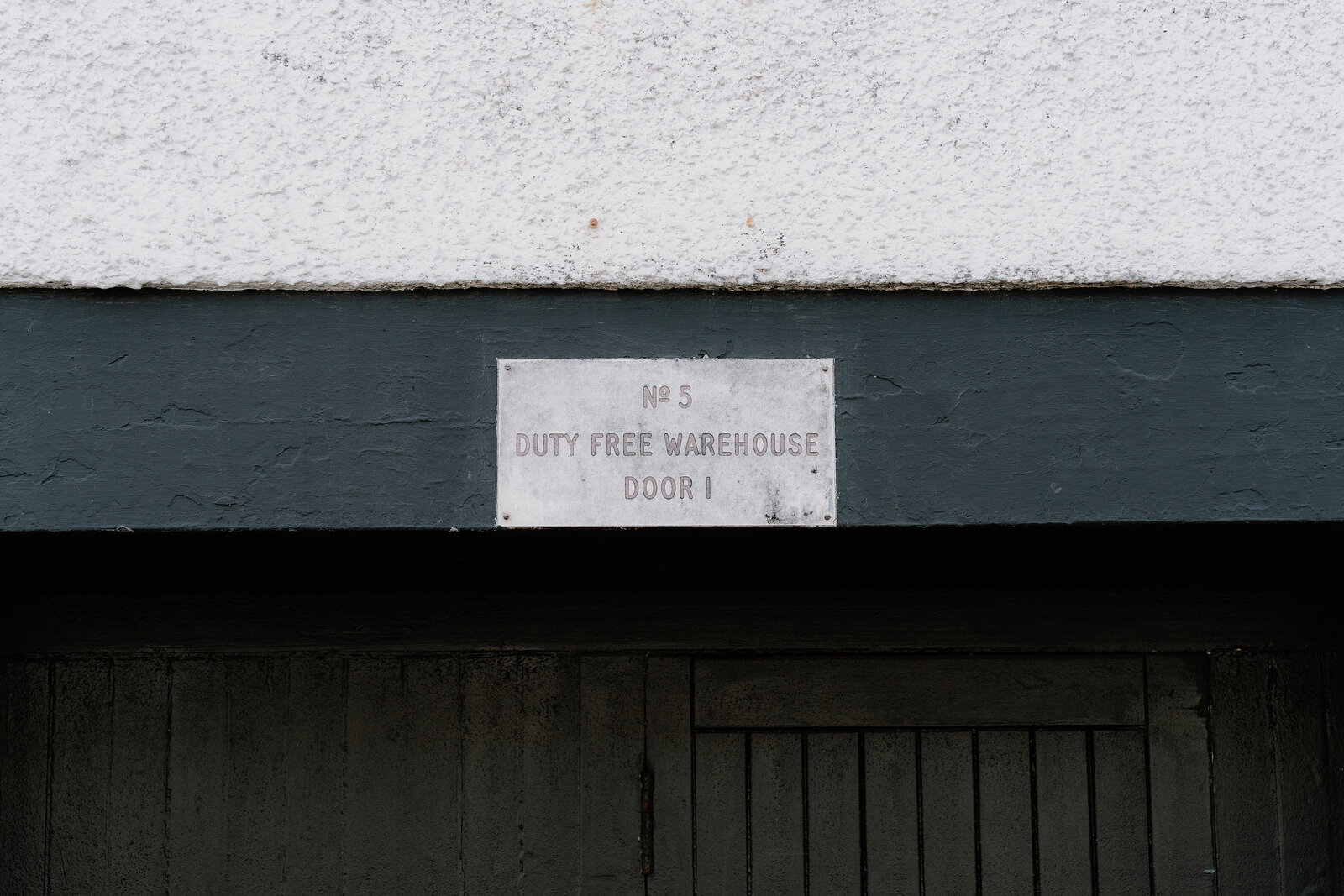 A plaque reading "No.5, Duty Free Warehouse, Door 1" is fixed above a wooden door.