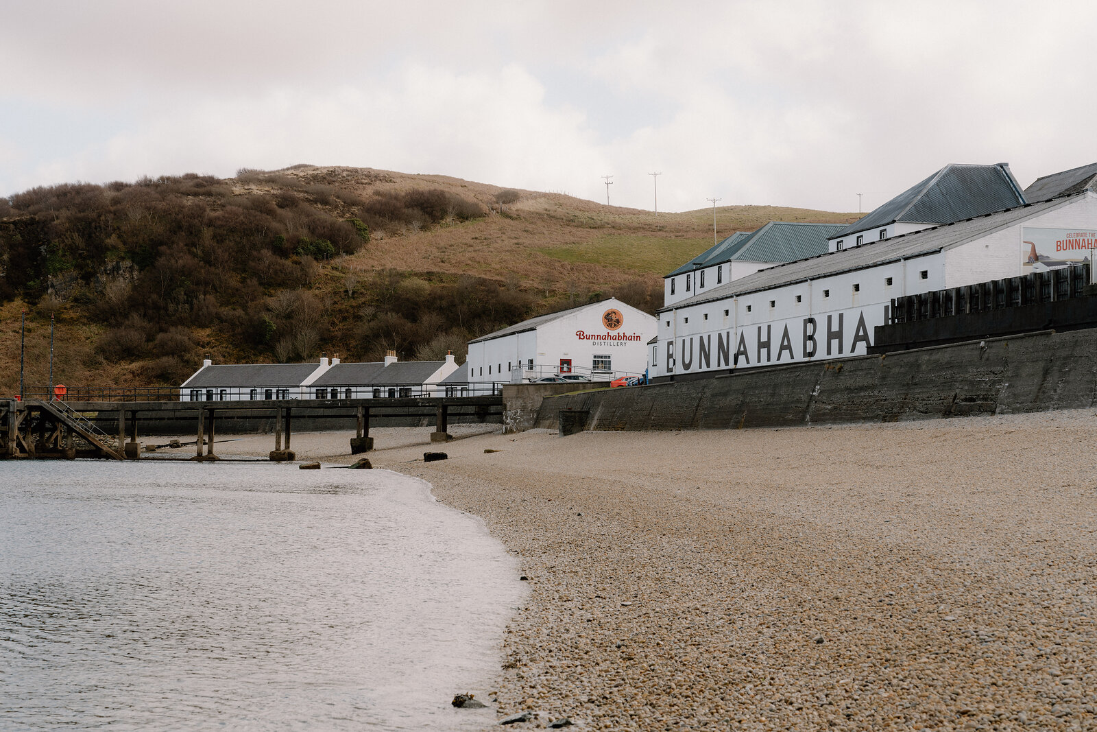 Bunnahabhain's lettering stretches across whitewashed buildings beside a pebble beach.