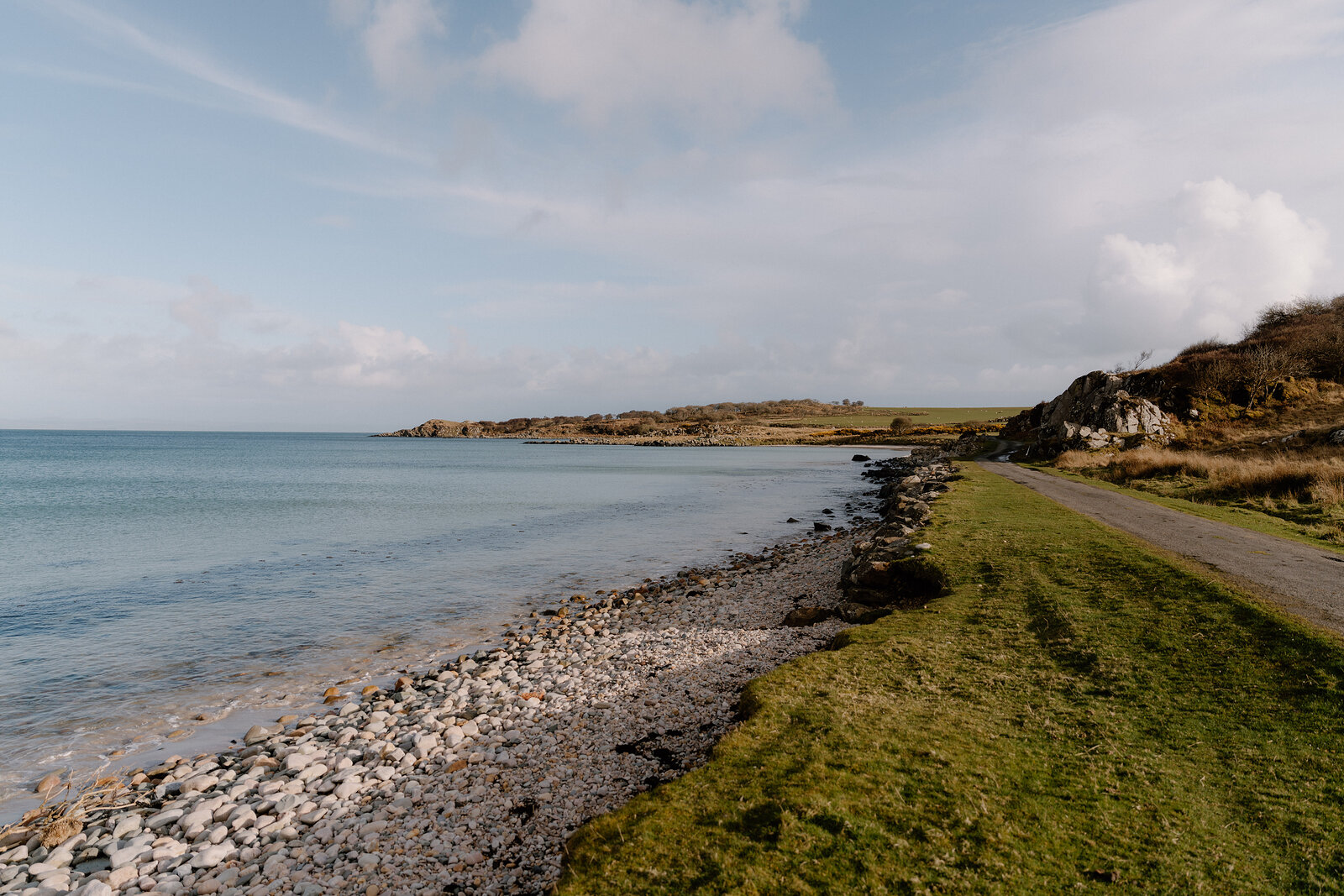 A single-track road runs along a rocky coastline beside calm water.