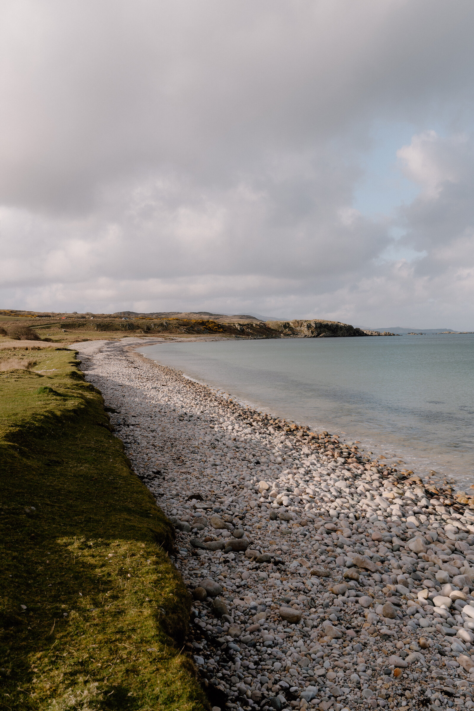 A pebble beach curves along the shore beneath low hills.