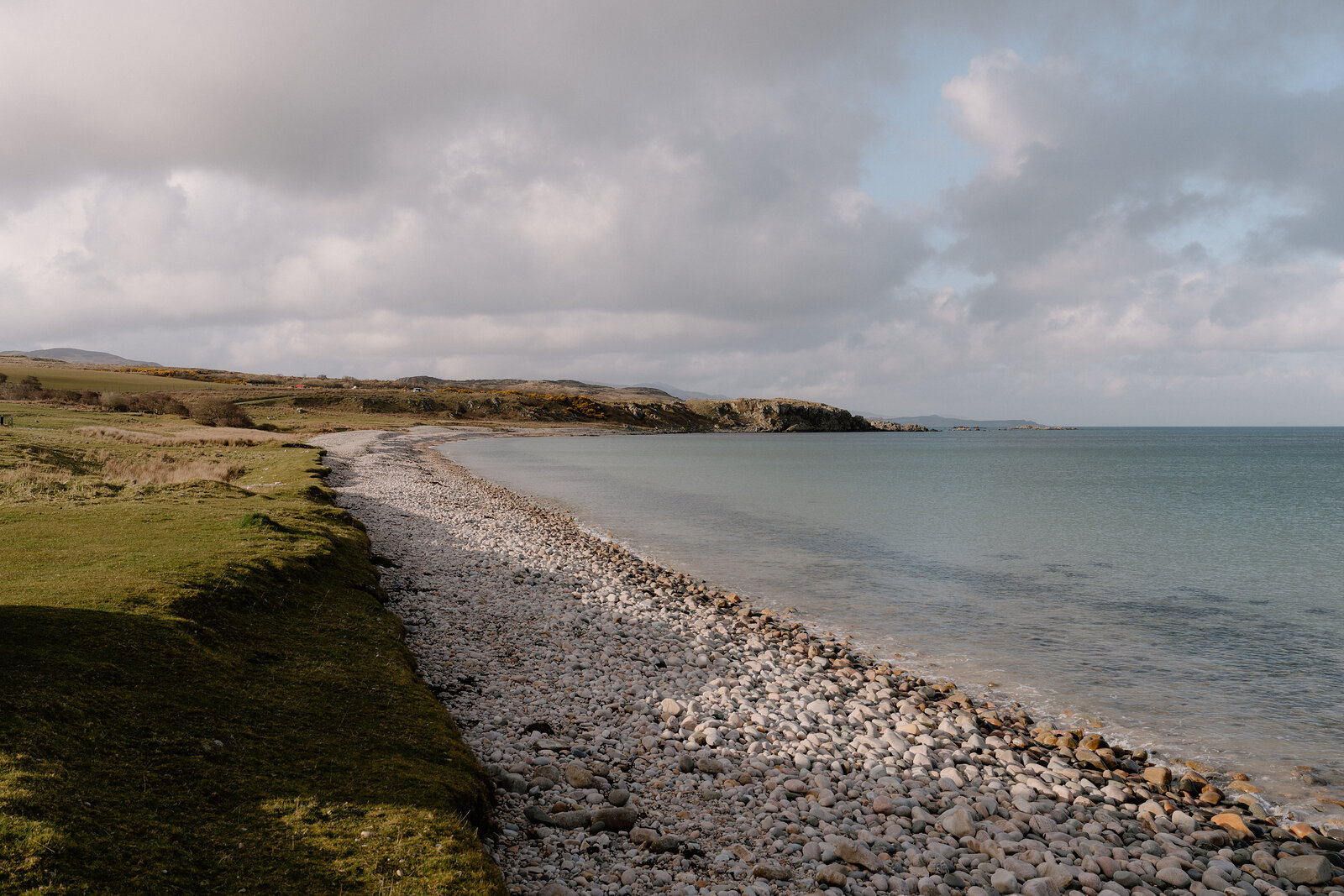 A pebble beach curves beside calm turquoise water.