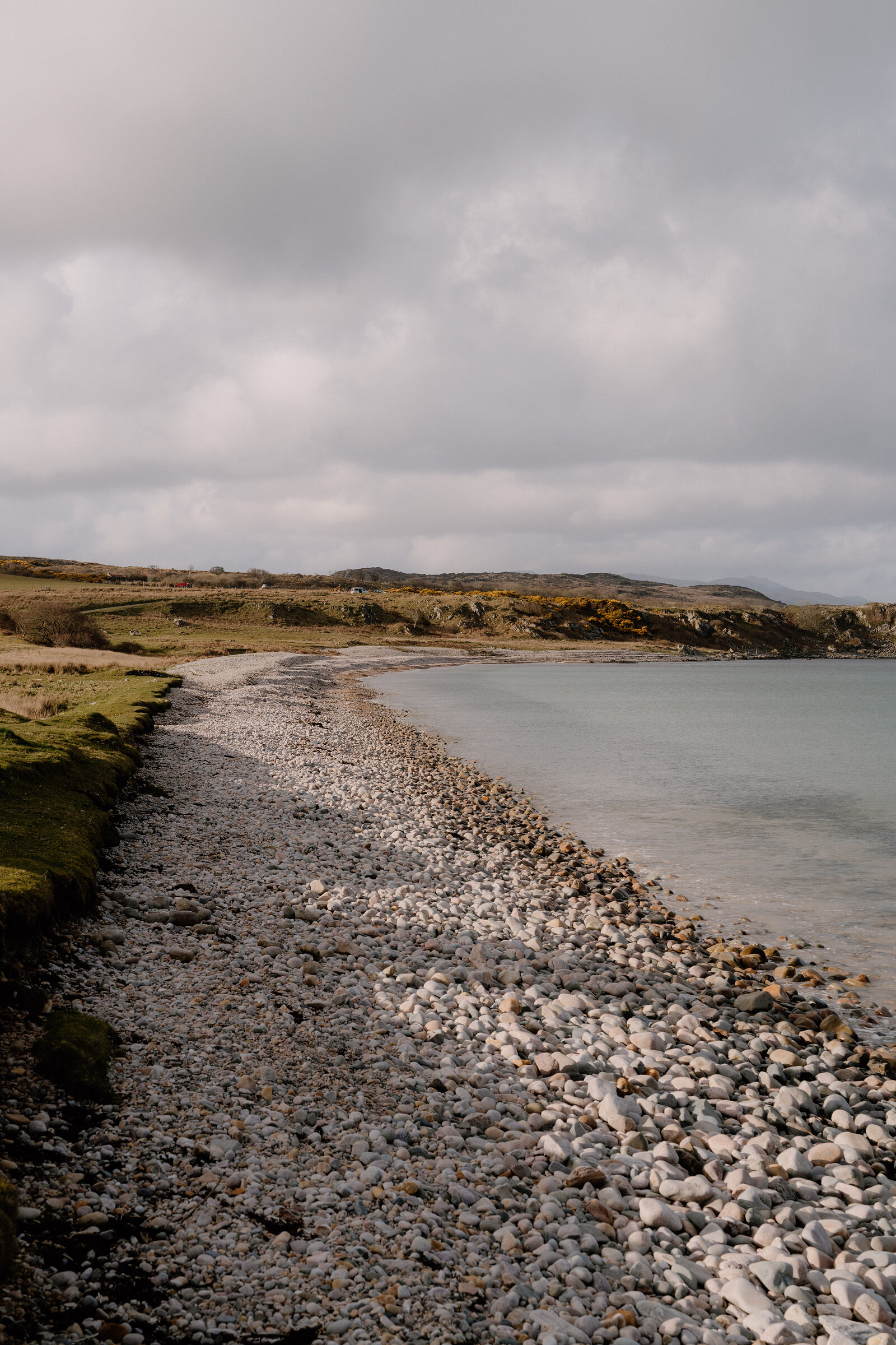 A pebble beach stretches along the shore beneath a cloudy sky.