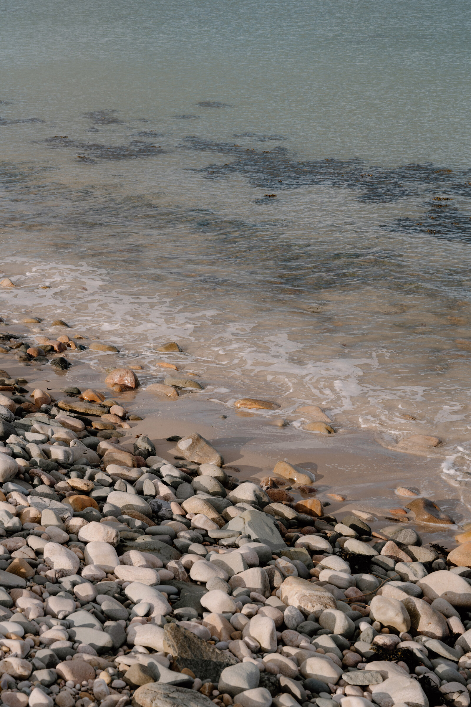 Smooth pebbles line the shore where gentle waves meet the sand.