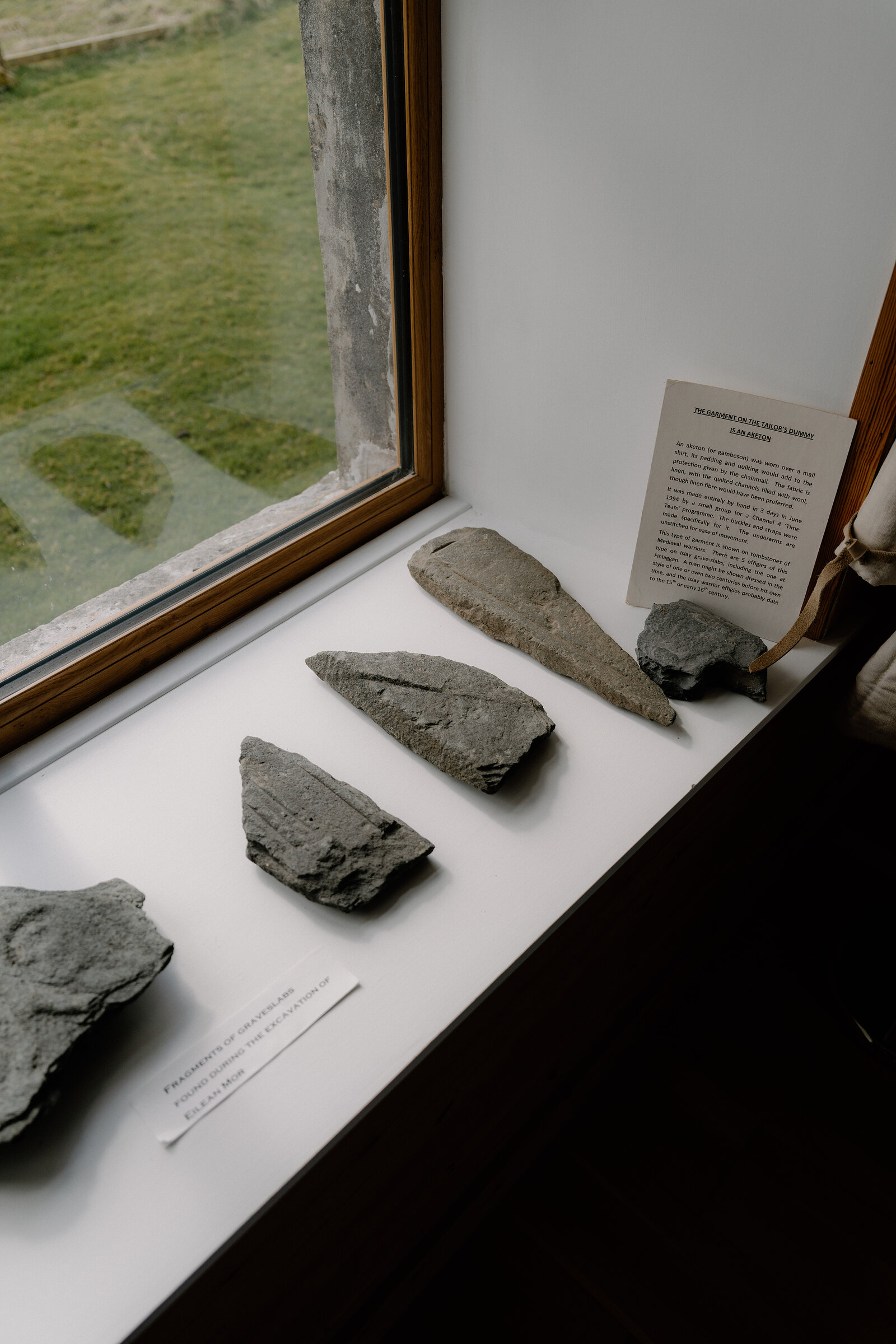 A museum display case holds several carved stone fragments beside descriptive cards.