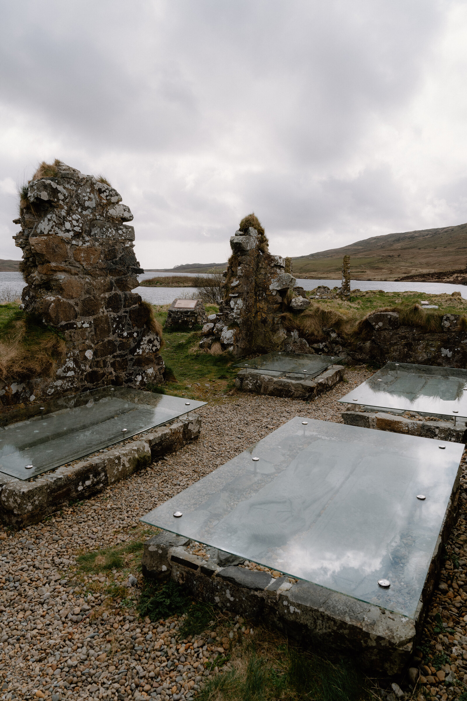 Glass-covered grave slabs sit among the ruined chapel walls at Finlaggan, overlooking the loch.