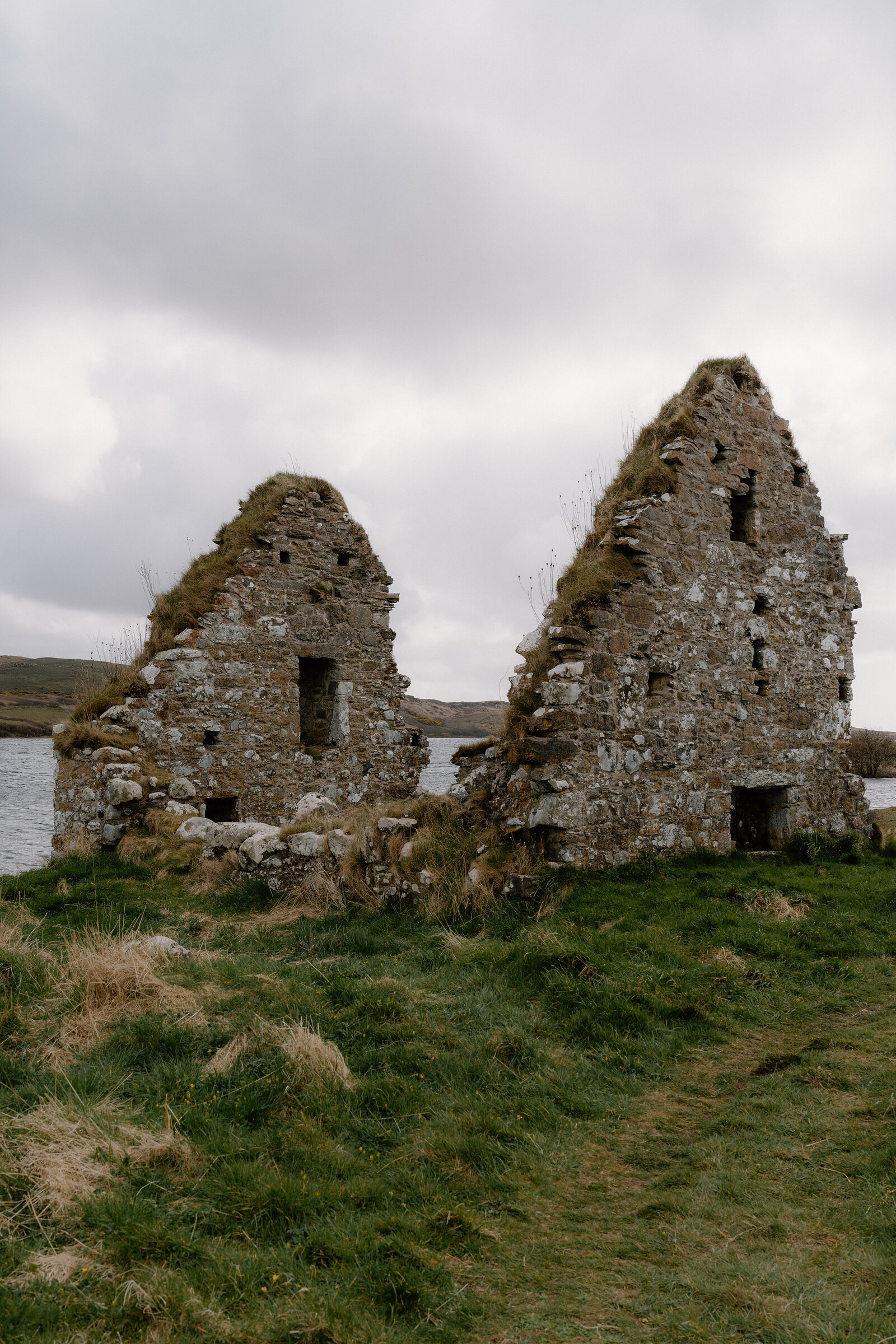 The gabled ruins of a stone chapel rise beside a loch at Finlaggan.