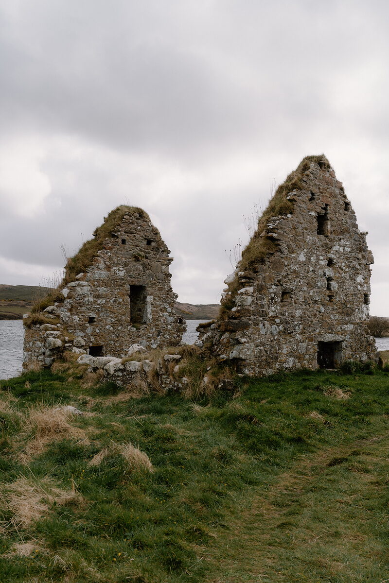 The gabled ruins of a stone chapel rise beside a loch at Finlaggan.