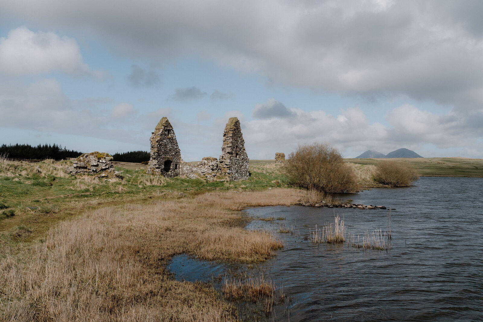 The ruined chapel walls of Finlaggan stand beside a loch, the Paps of Jura visible on the horizon.