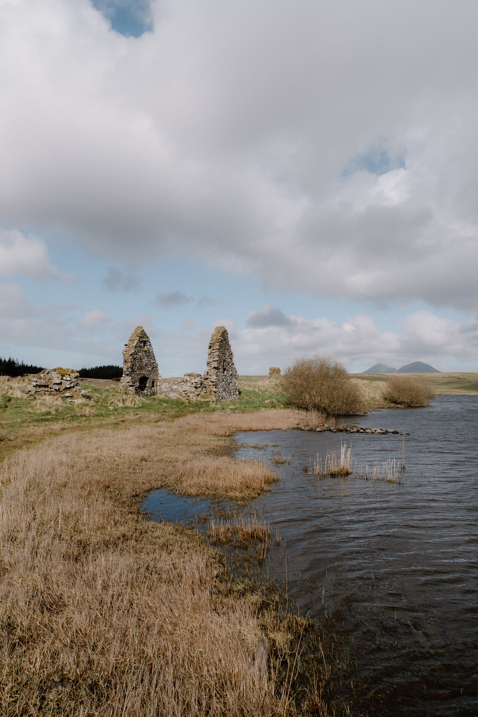 The ruined chapel walls of Finlaggan rise beside a loch, the Paps of Jura on the skyline.