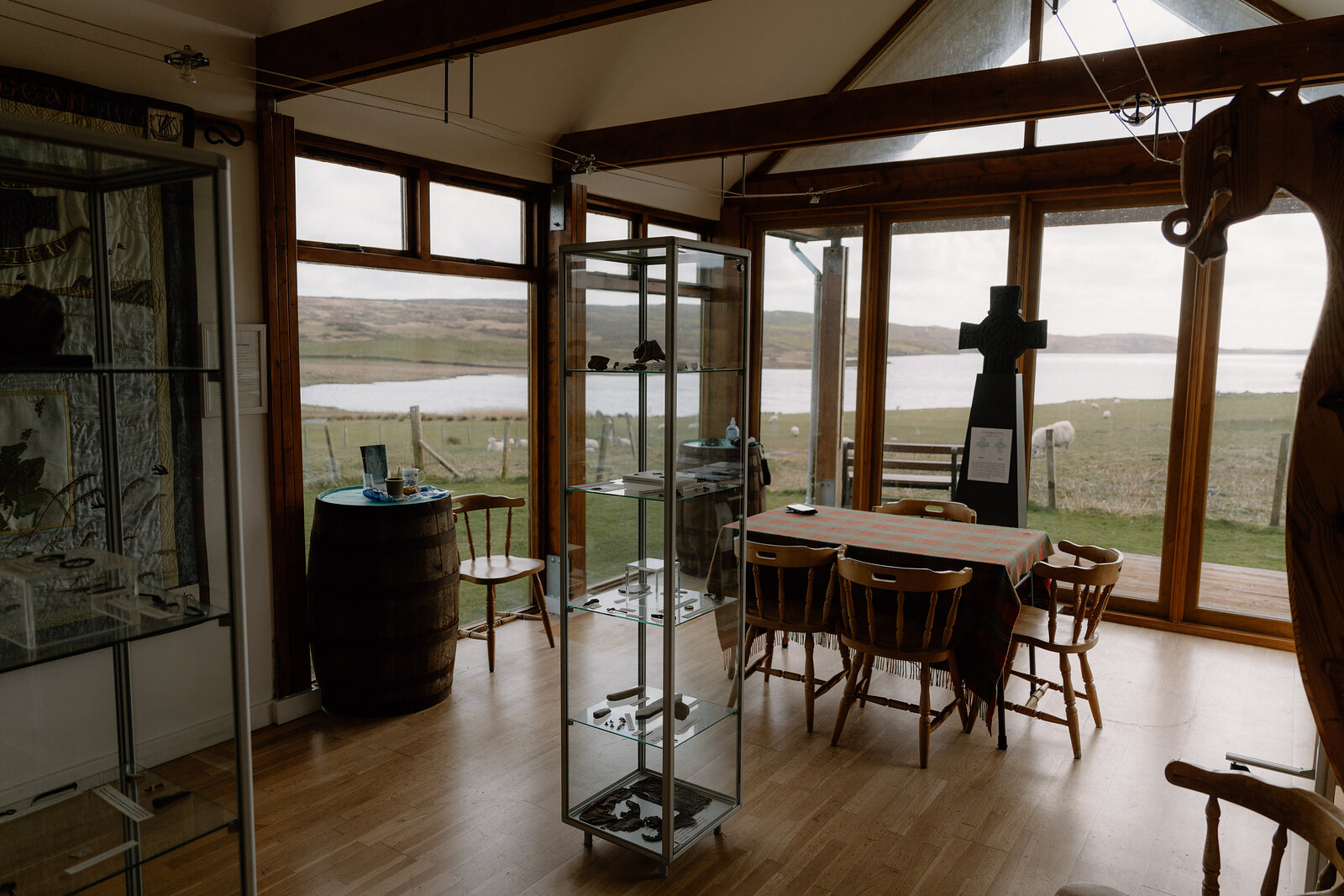 Glass display cases stand in a lochside room furnished with a carved stone cross and dining table.