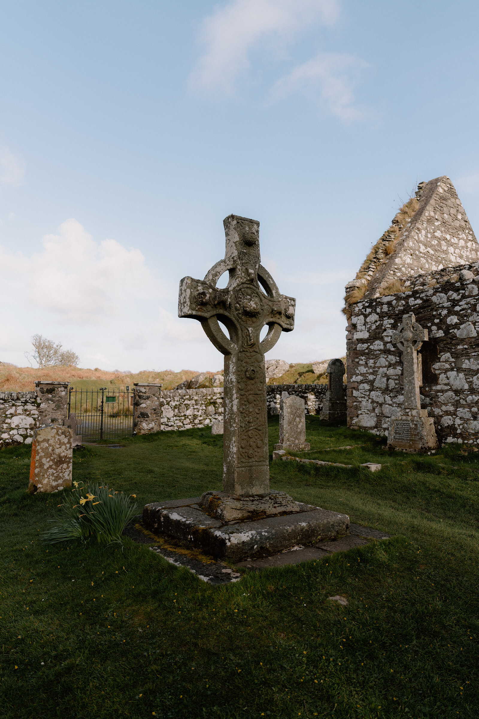 A weathered carved cross with a ringed head stands in a grassy churchyard.