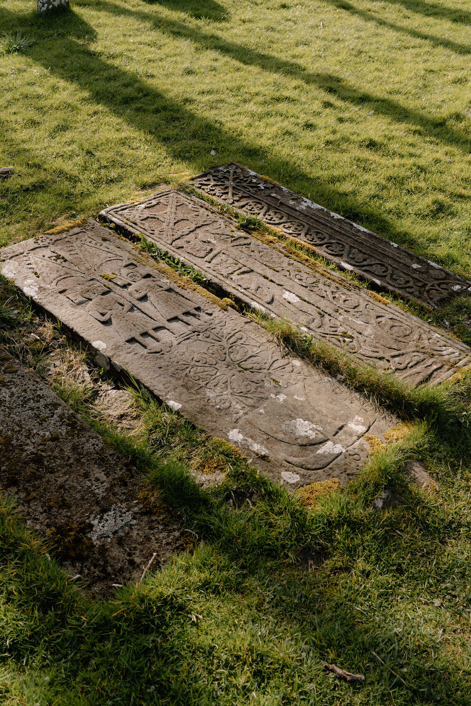Carved medieval grave slabs lie flat in the grass of a ruined churchyard.