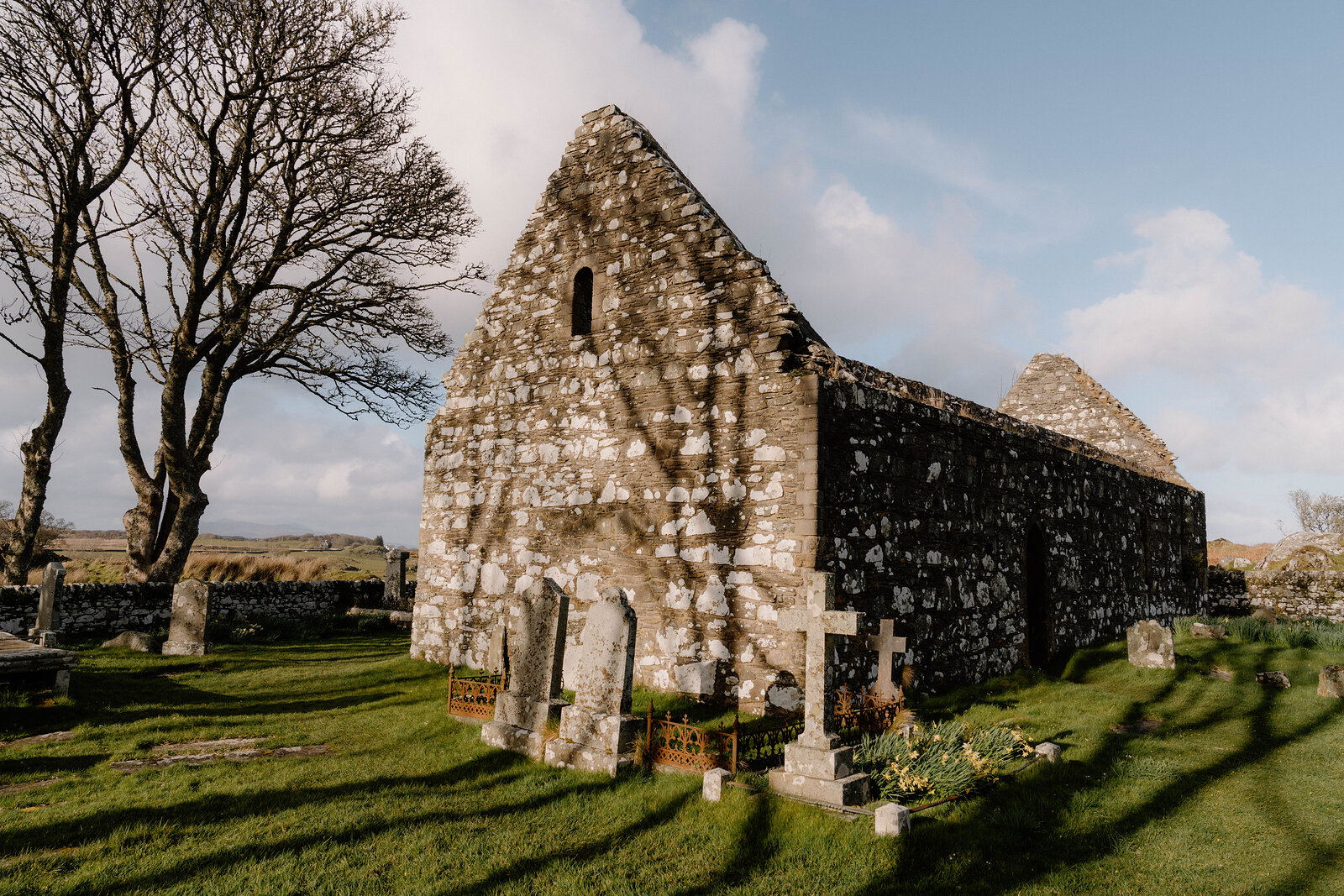 The roofless gable walls of a ruined stone chapel stand among gravestones.