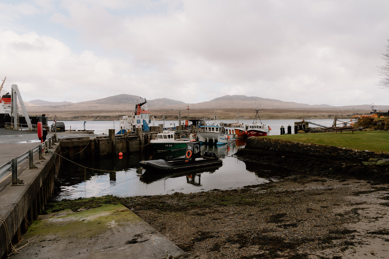Fishing boats are moored at a small stone harbour beneath distant hills.