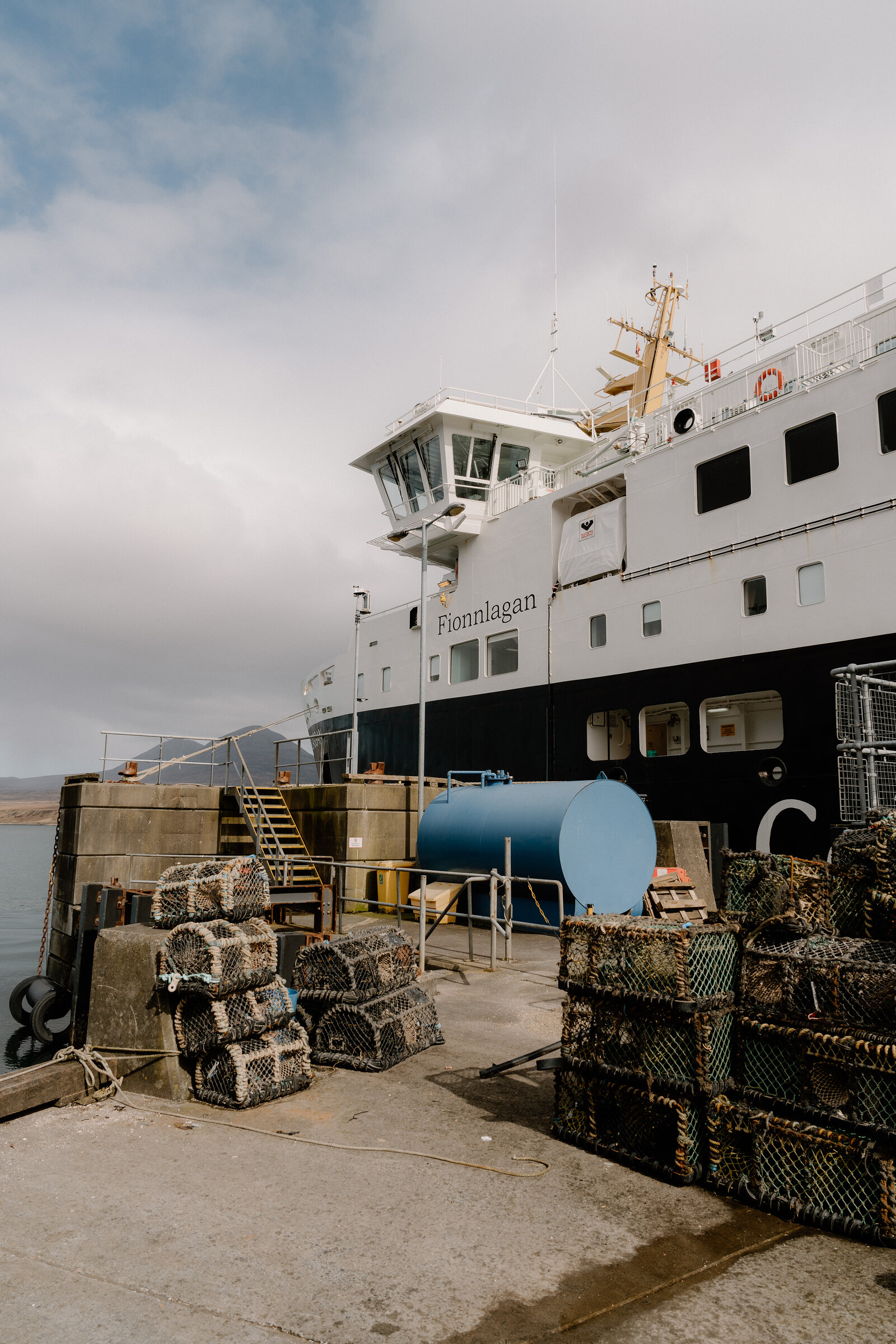 The Caledonian MacBrayne ferry Fionnlagan is moored at a stone jetty beside stacks of lobster creels.