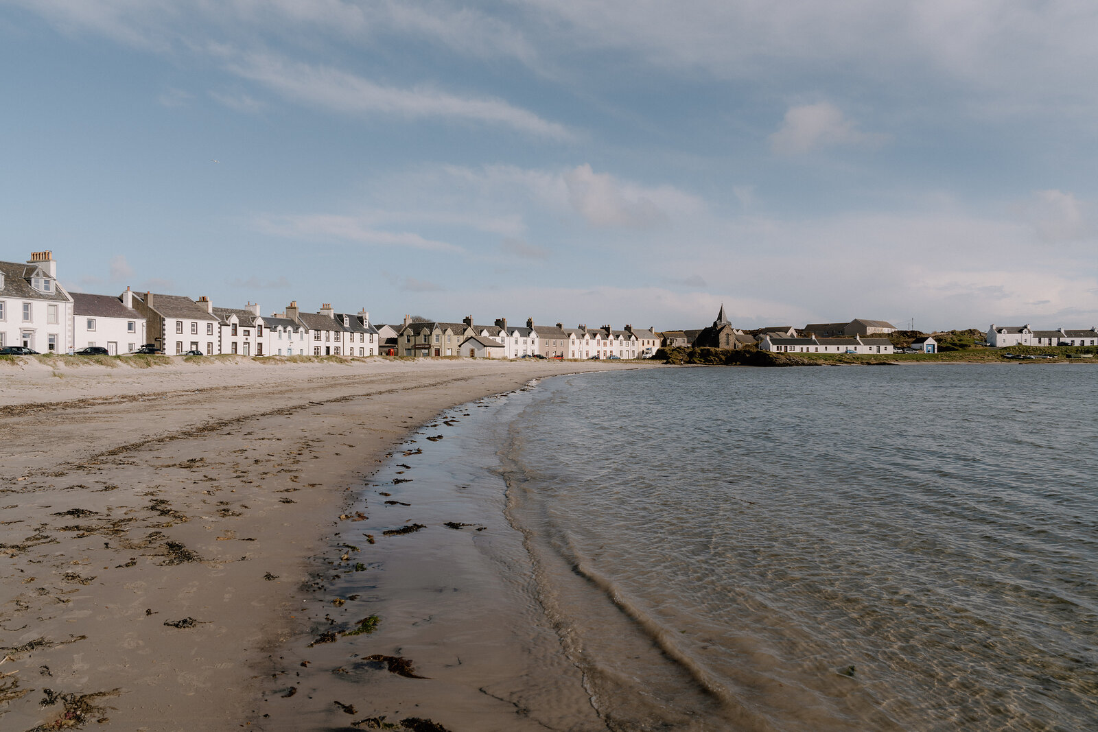 White terraced houses curve along a sandy beach in an Islay village.