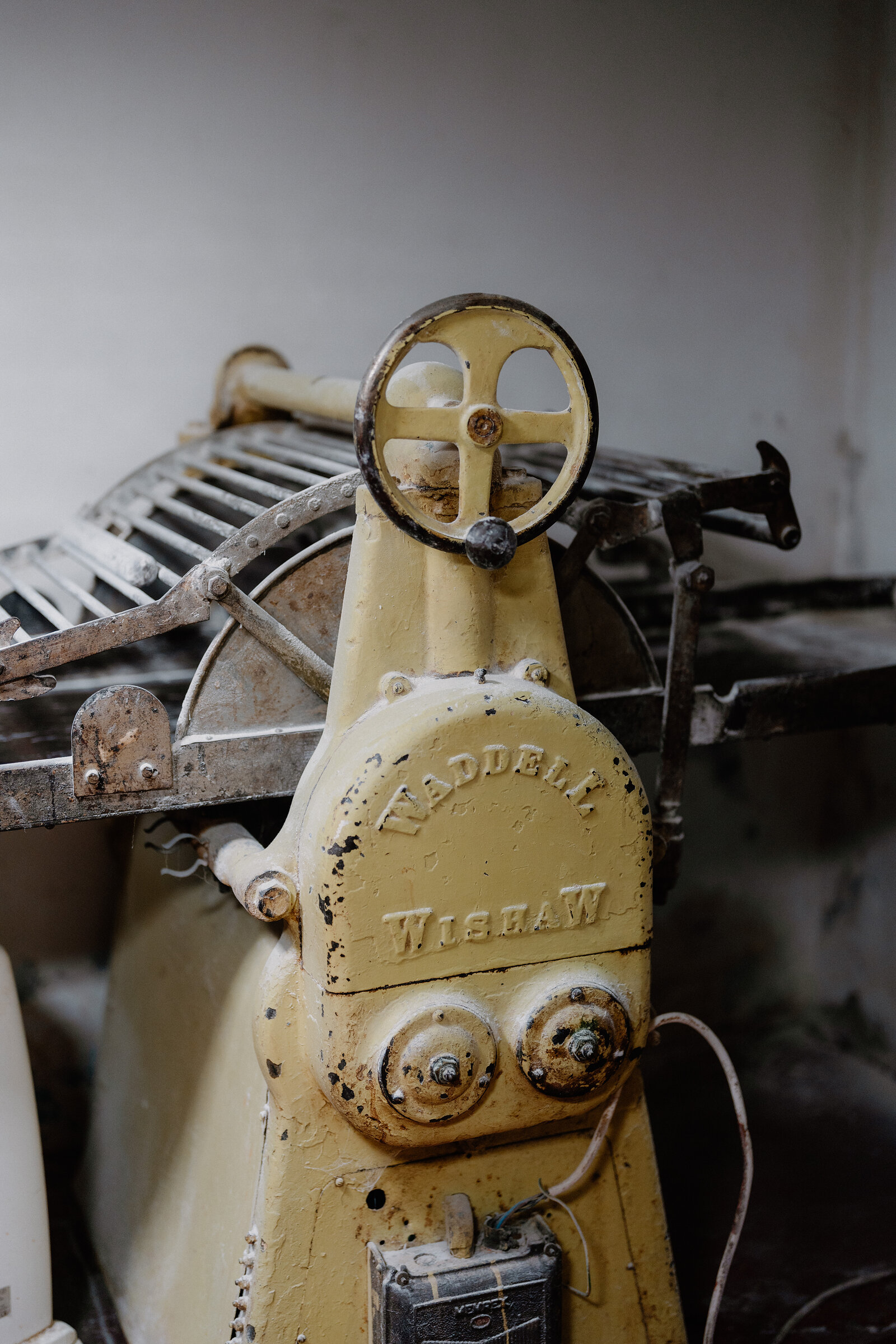 A vintage machine stamped "WADDELL WISHAW" has a wheel handle and a metal wire frame, weathered paintwork showing its age.