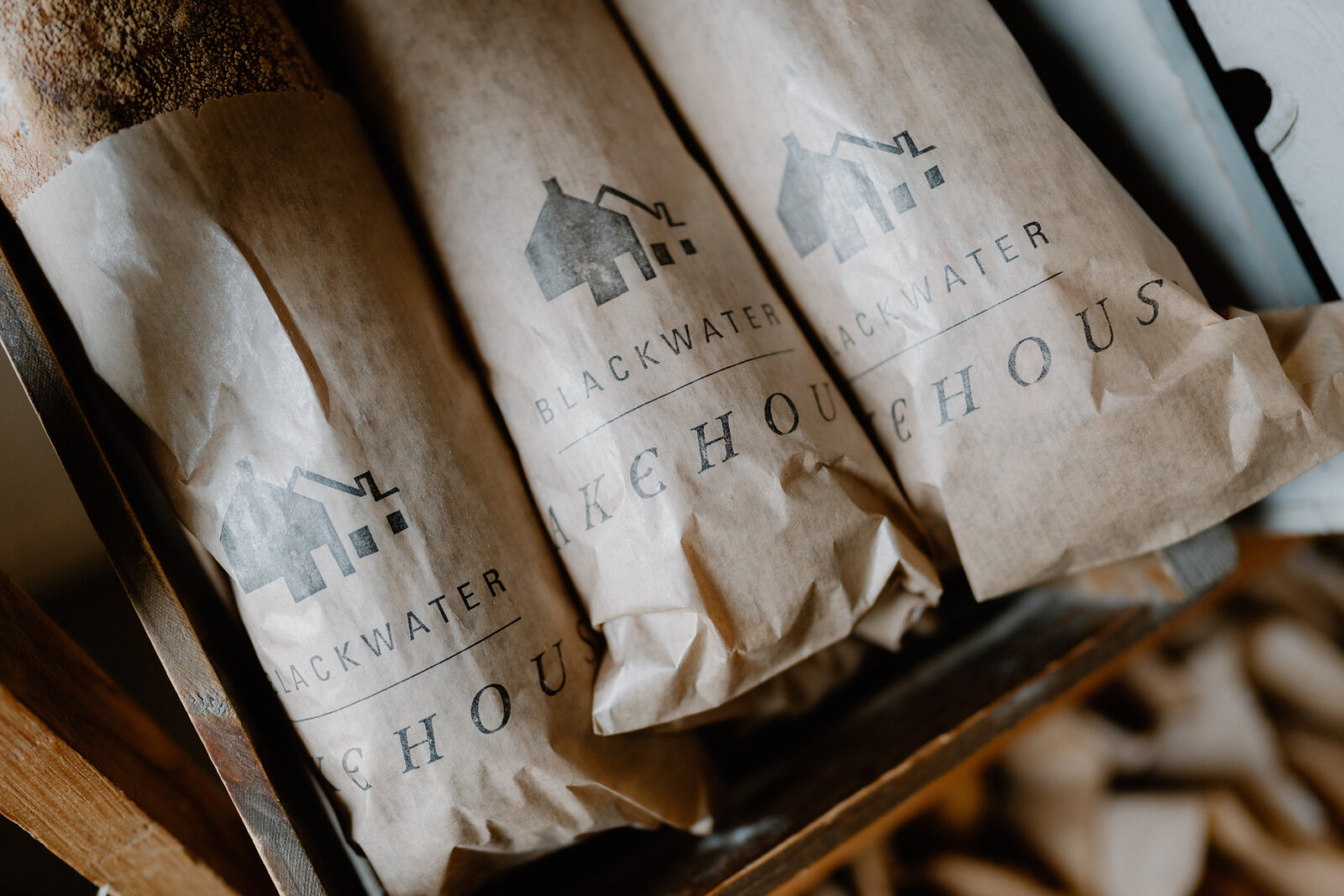 Paper bags printed "Blackwater Bakehouse" lie stacked on a shelf, a wrapped loaf visible in the gap beside them.