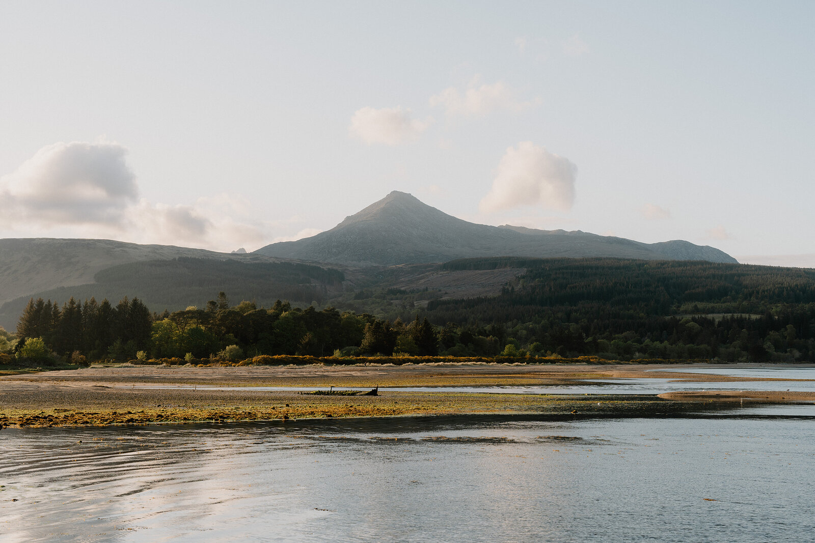 A conical mountain rises beyond a calm bay, a small boat resting on the exposed sand at low tide.