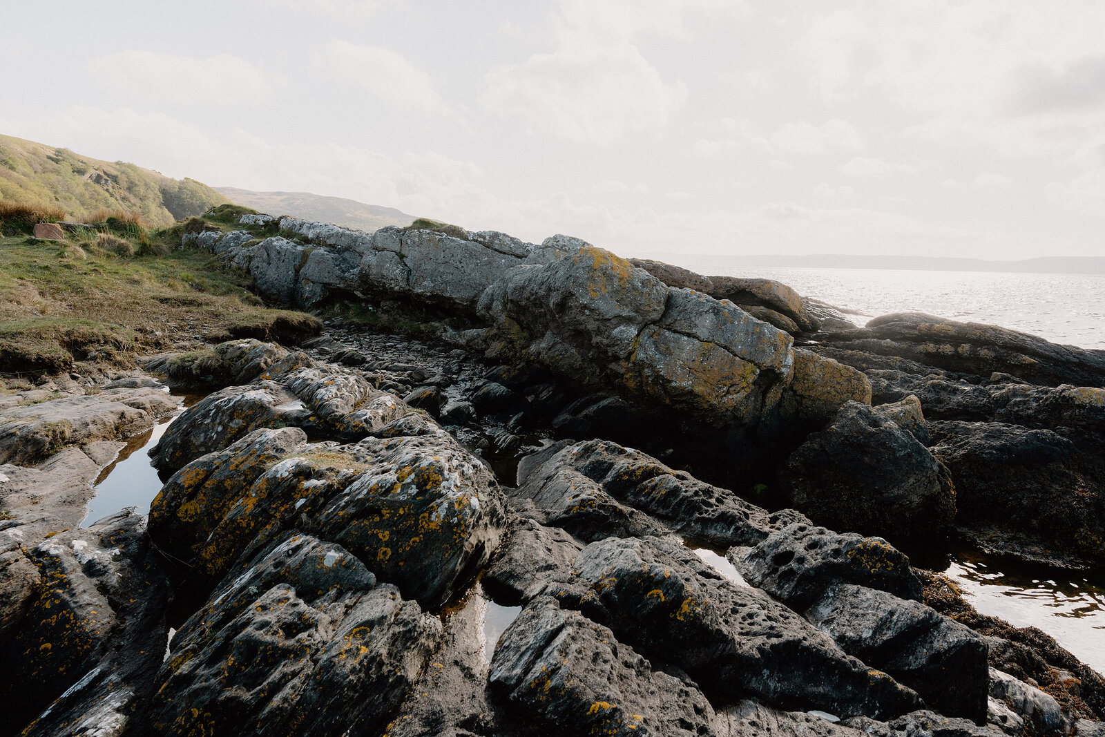 Lichen-streaked rock ledges form a natural causeway along a shoreline, tidal pools collecting in the hollows.