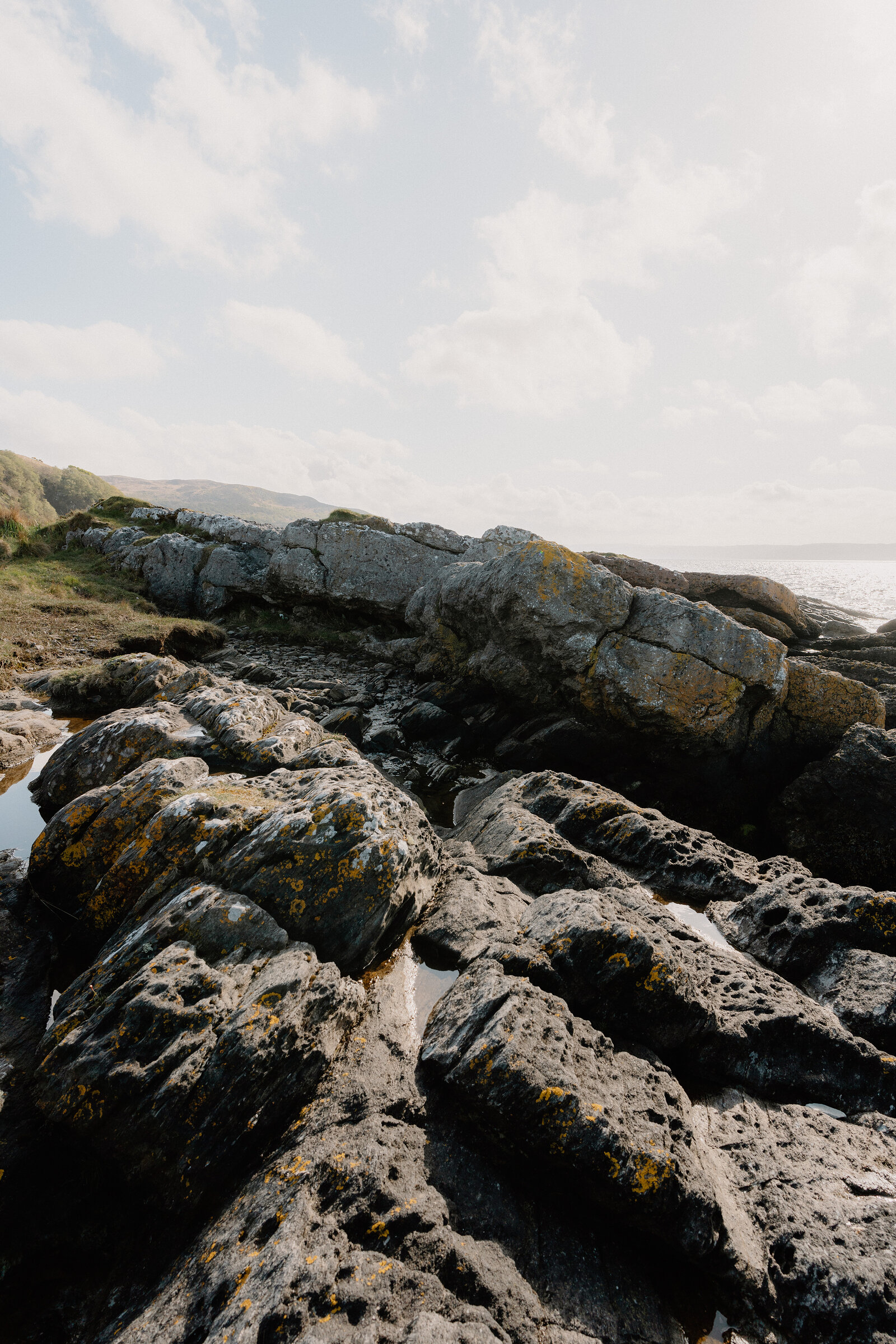 Lichen-streaked rock ledges form a natural causeway along a shoreline, tidal pools collecting in the hollows.