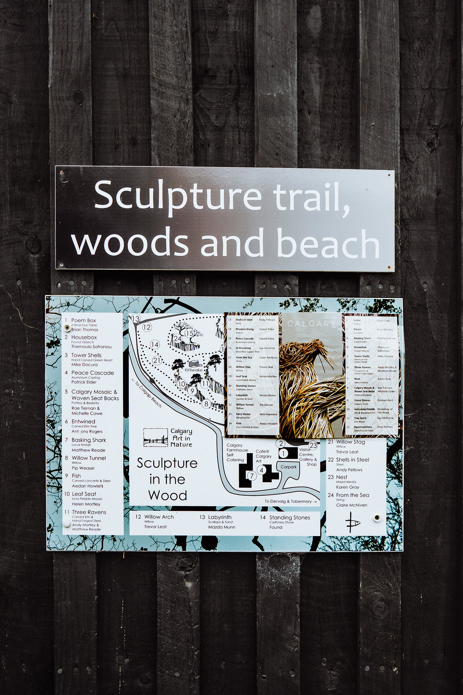 A sign reading "Sculpture trail, woods and beach" hangs above a map titled "Sculpture in the Wood, Calgary Art in Nature" listing numbered artworks.