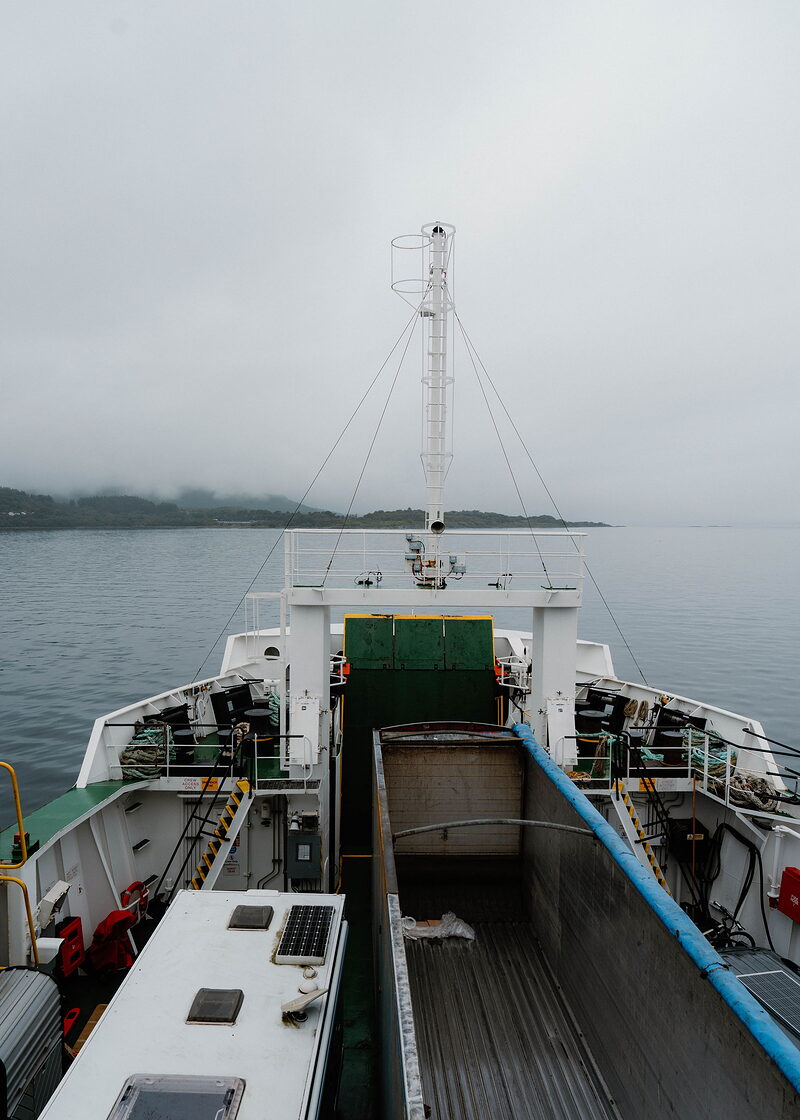 An upright frame over the ferry's bow and car deck towards Mull, low cloud lying along the coast ahead.