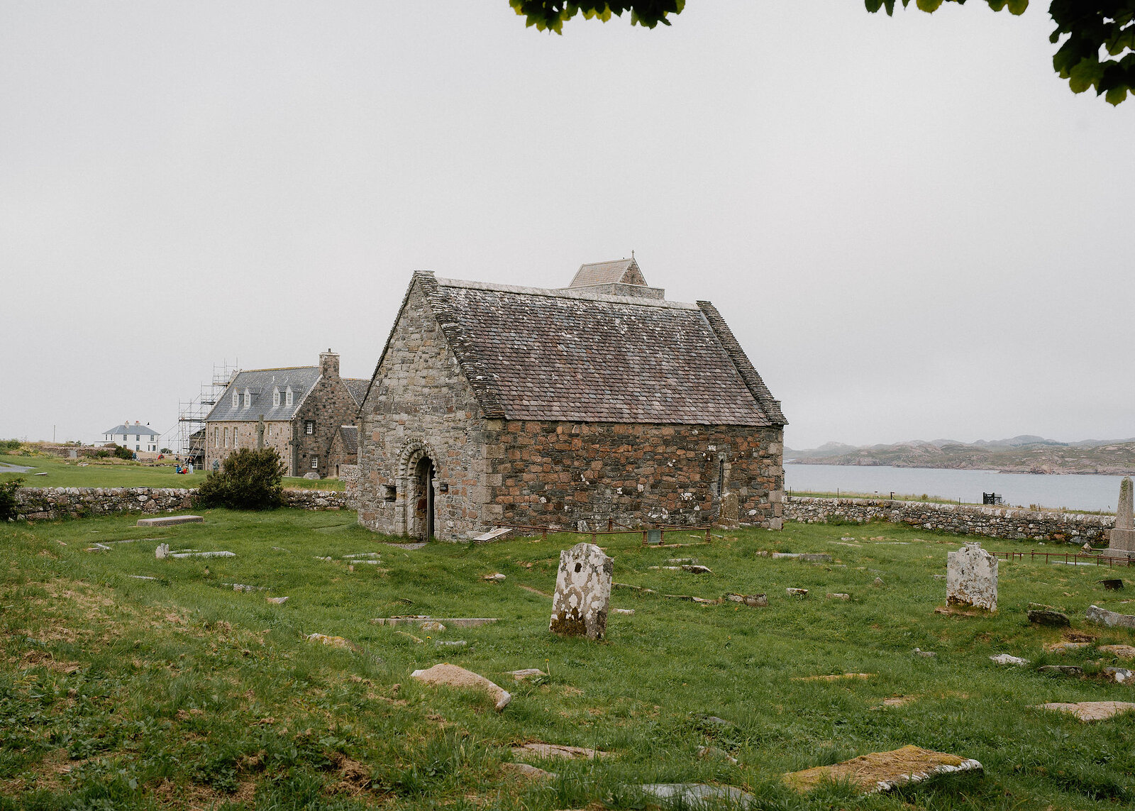 A landscape view of the chapel among old gravestones, the sound and the Mull shore to the right.