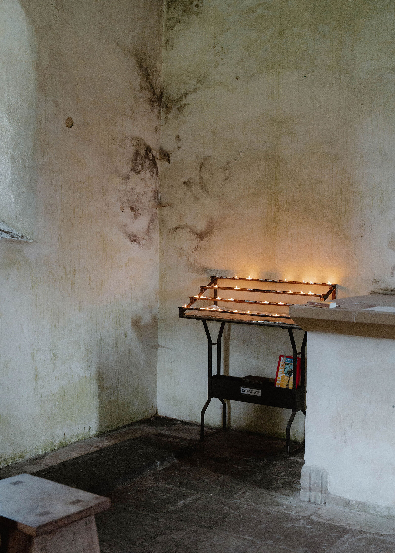 Candles burning on an iron stand in the corner of the whitewashed chapel, damp stains on the walls.