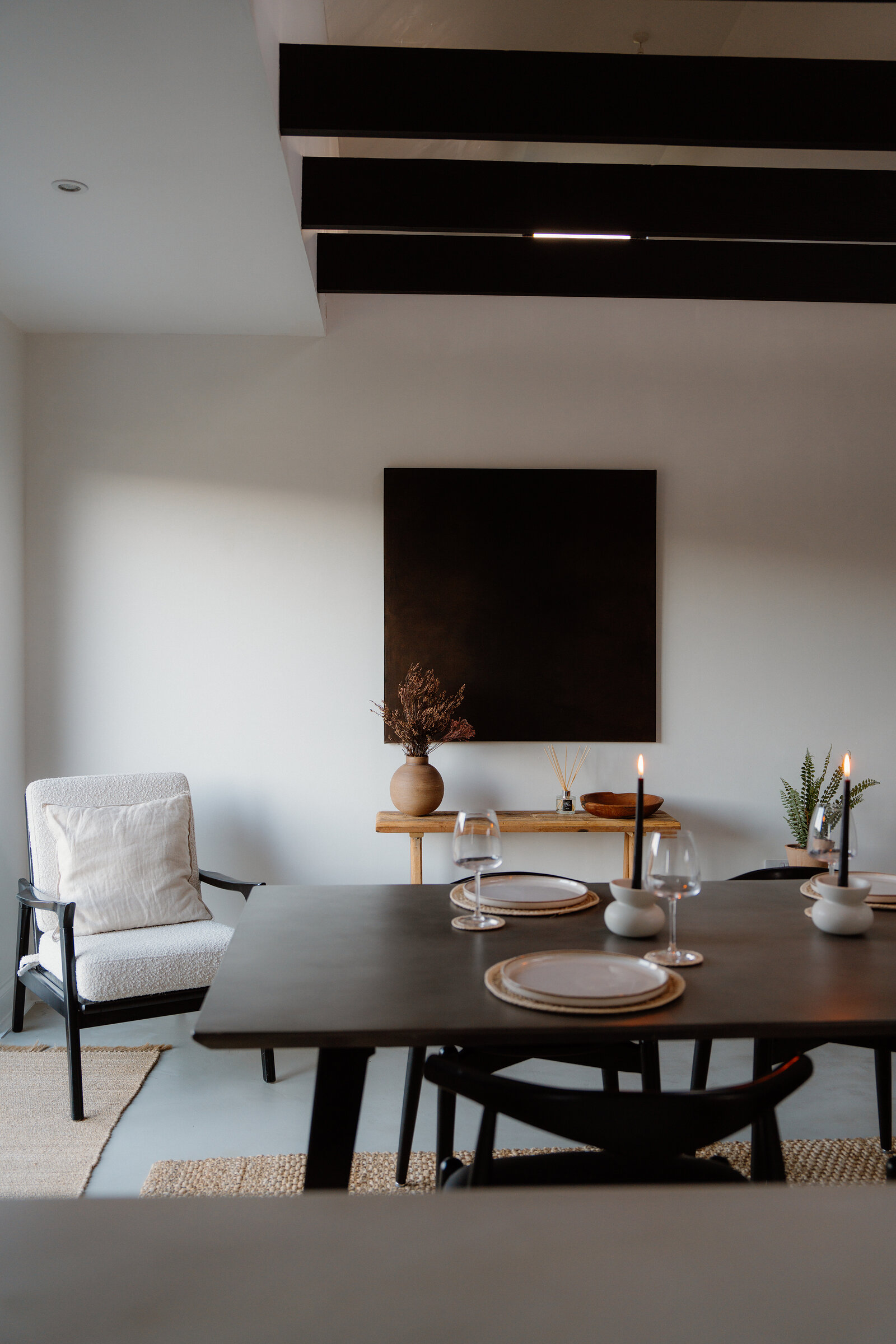 A dining table is set with candles and wine glasses in a black-beamed room.