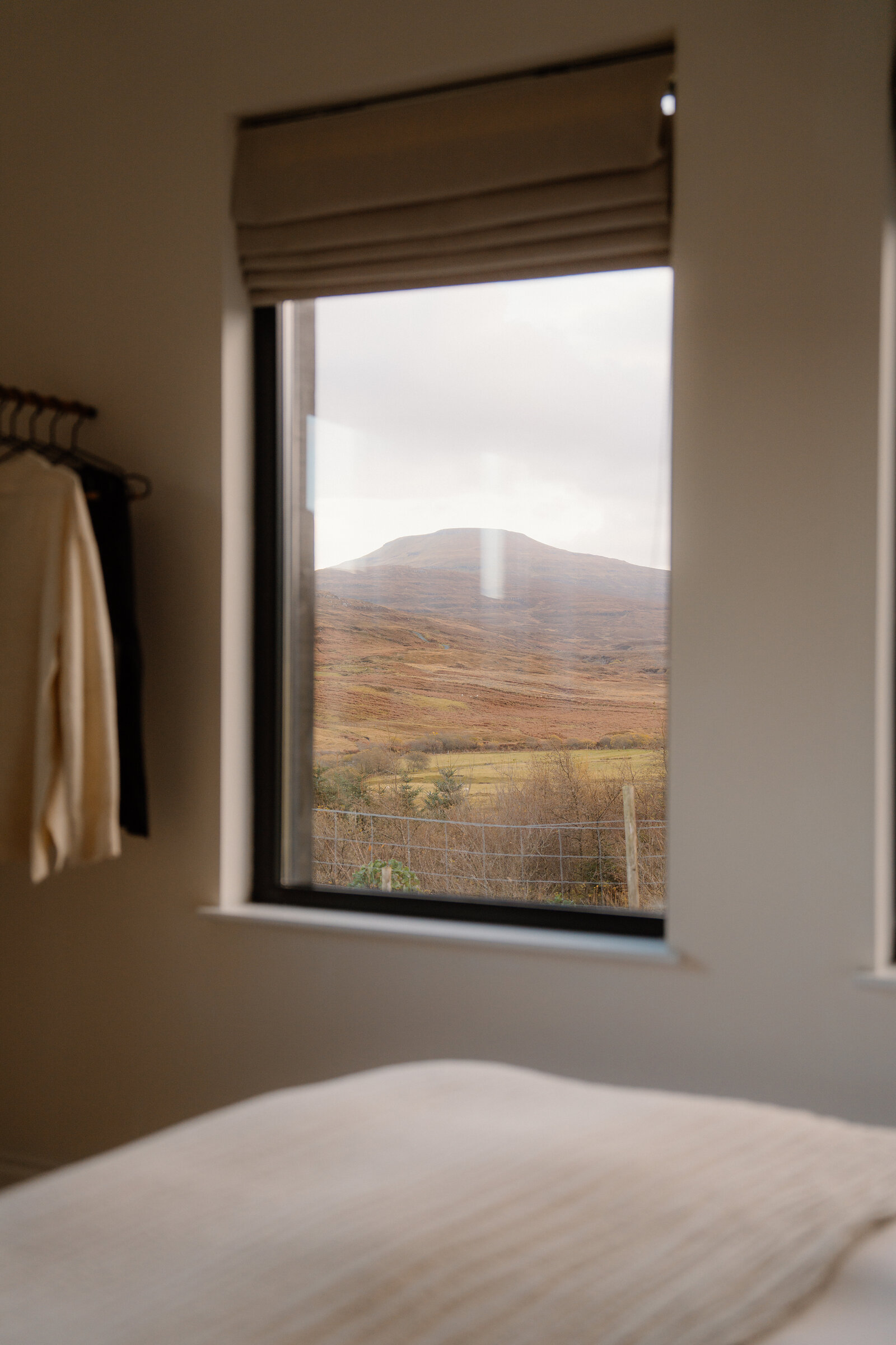 A window looks out over moorland hills beside a hanging clothes rail.