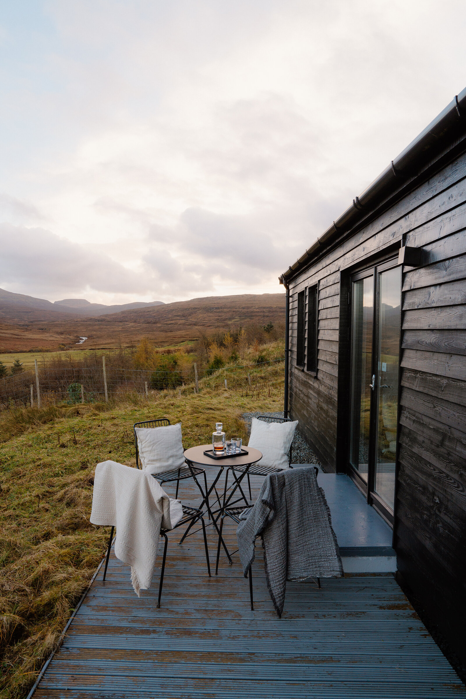 A bistro table and chairs sit on a deck overlooking moorland hills.