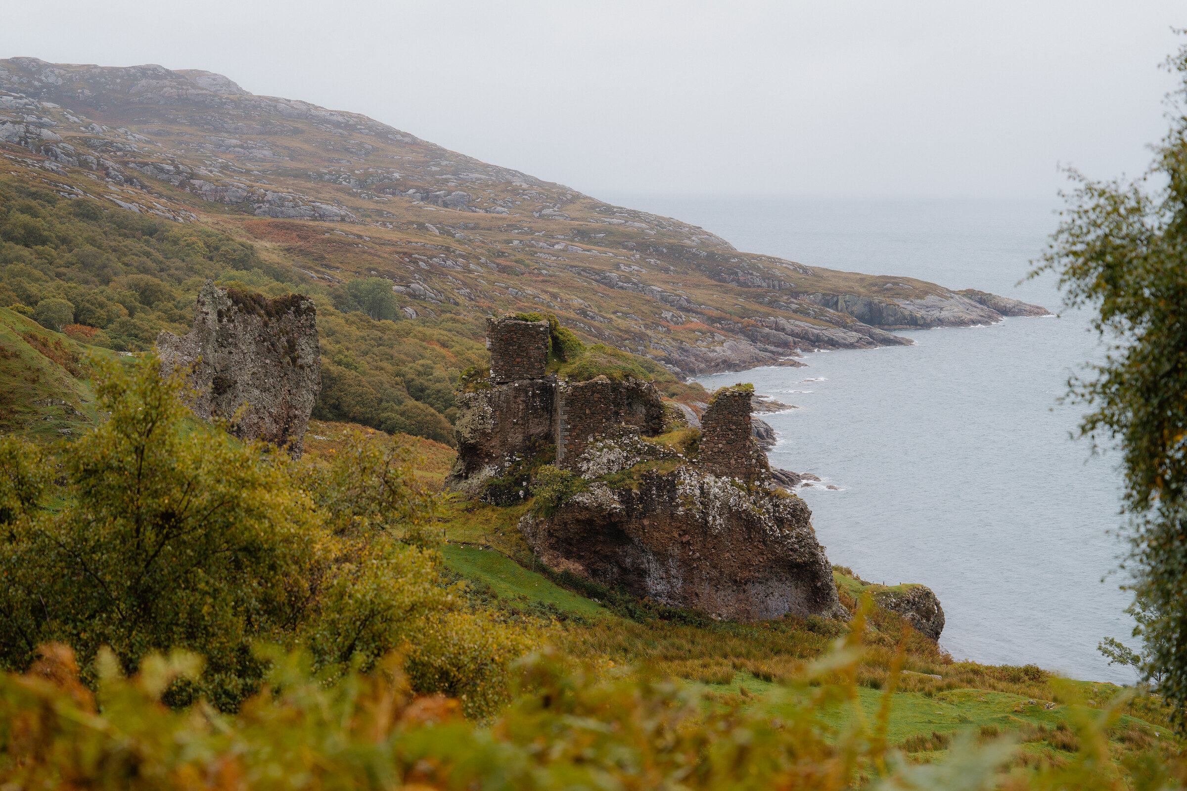A ruined stone castle crowns a rocky headland above the sea.